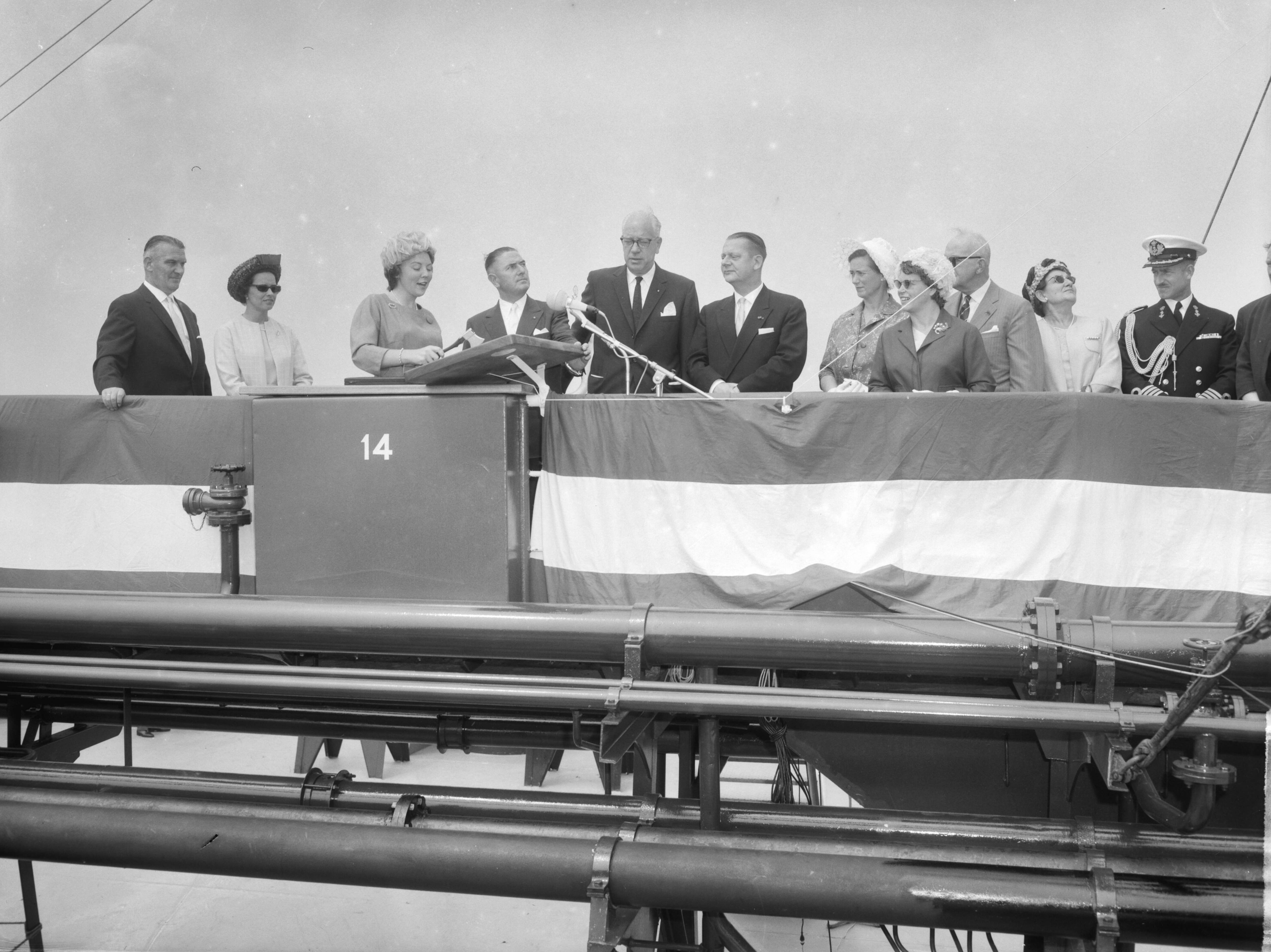 Fotocollectie Anefo — Prinses Beatrix doopte de grootste tanker "Esso Den Haag" op de Noordzee. Prinses Beatrix hakt met een bijltje een touw door, rechts naast haar Cornelis Verolme, naast hem de president-directeur van Esso Nederland, C.R. Smit. Links van de prinses haar particuliere secretaresse mej. M.C.C. Wijnen — Foto: Bilsen, Joop van / Anefo. Licentie: Set B: Rechtenvrij / Publiek Domein. Bron: Nationaal Archief. http://hdl.handle.net/10648/aa3db1f4-d0b4-102d-bcf8-003048976d84