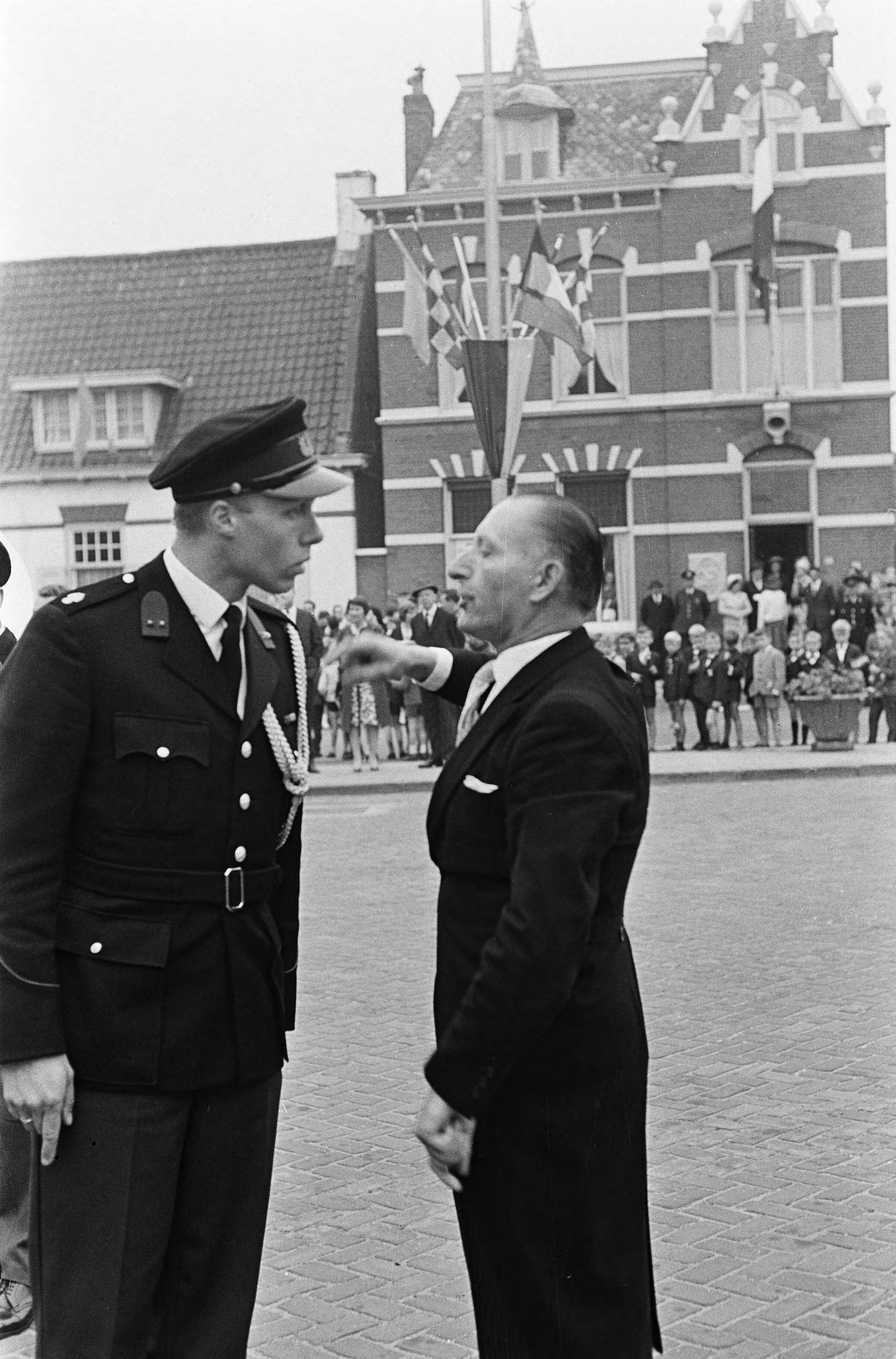 Koningin Juliana onthult het Van Gogh-monument in Zundert — Een politieagent in discussie met een aanwezige — Foto: Fotograaf Onbekend / Anefo. Licentie: Set B: Rechtenvrij / Publiek Domein. Bron: Nationaal Archief. http://hdl.handle.net/10648/aa6af1be-d0b4-102d-bcf8-003048976d84