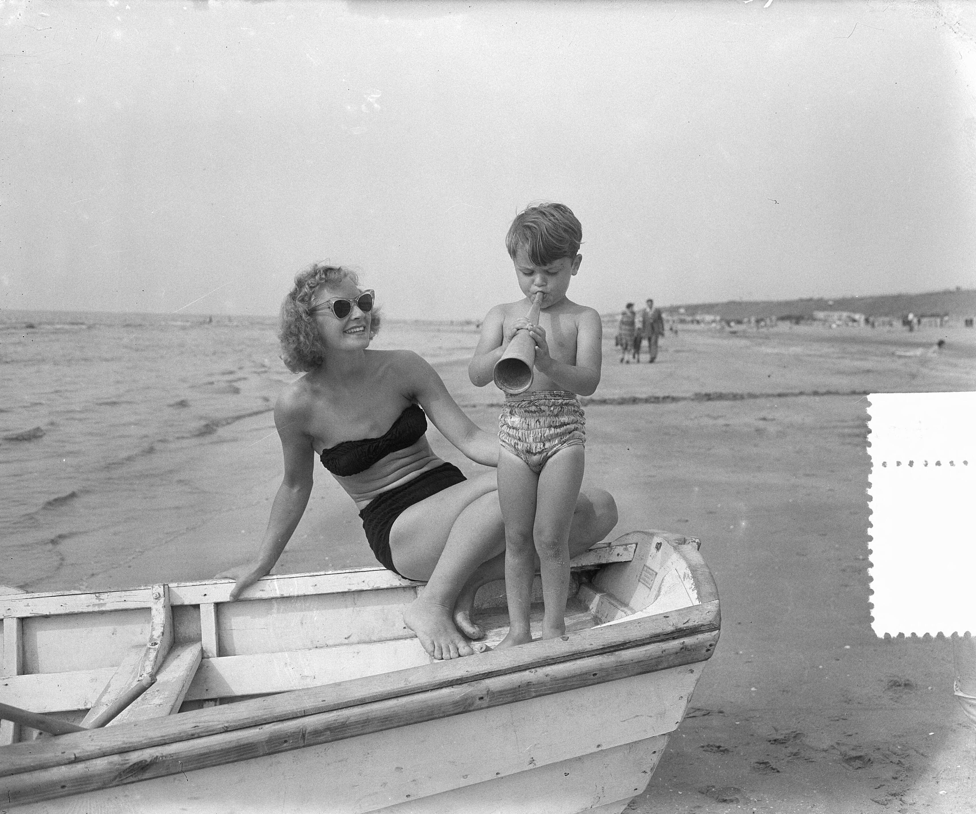 Fotocollectie Anefo — Zomerplaatjes aan strand van Zandvoort. Moeder en kind in roeiboot. Kind blaast op toeter — Foto: Pot, Harry / Anefo. Licentie: Set B: Rechtenvrij / Publiek Domein. Bron: Nationaal Archief. http://hdl.handle.net/10648/a90e5716-d0b4-102d-bcf8-003048976d84