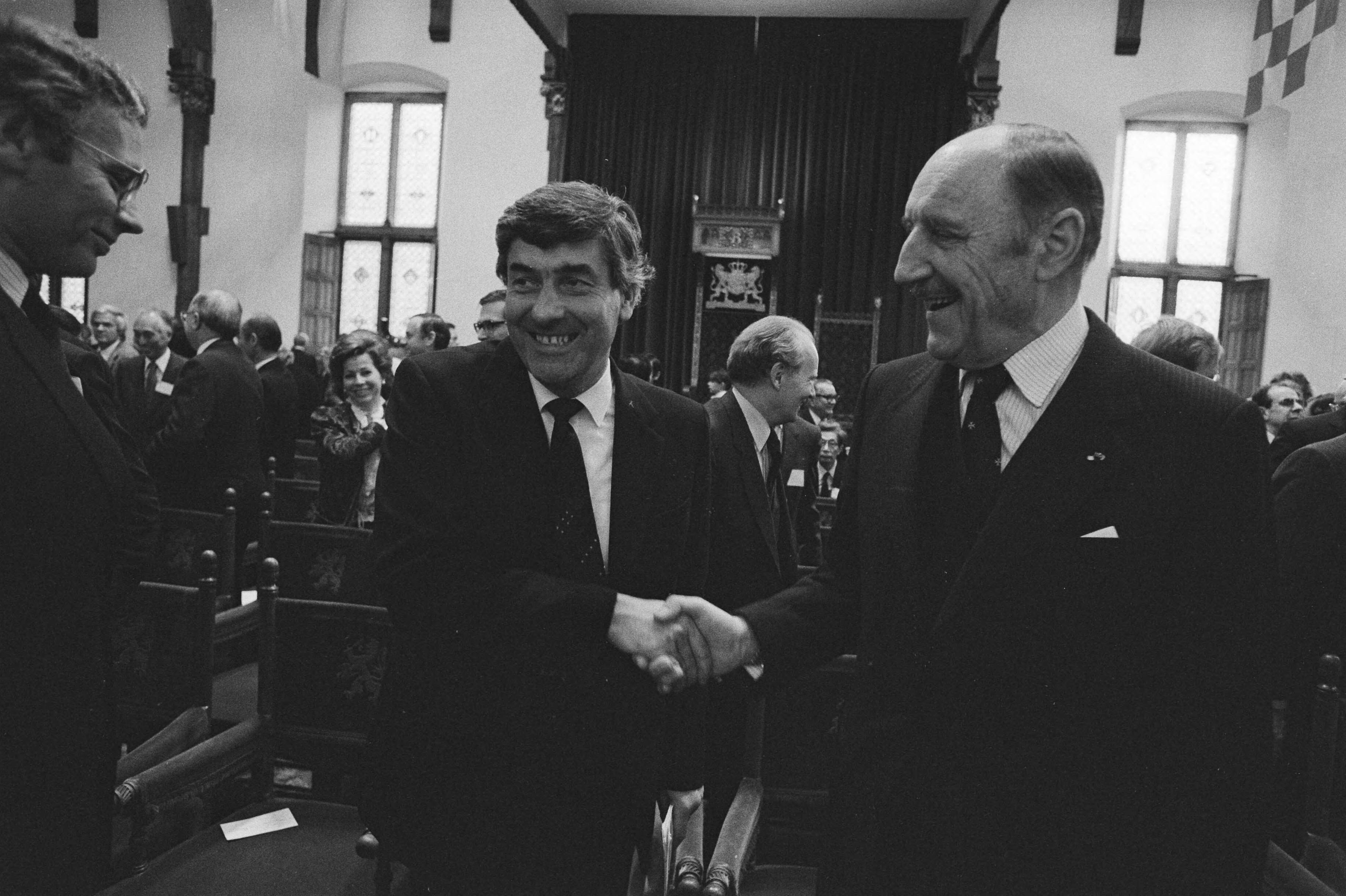 Noord Atlantische Assemble in Ridderzaal in Den Haag — Premier Lubbers (l) schudt secretaris-generaal Luns (NAVO) de hand; links minister Van den Broek — Foto: Bogaerts, Rob / Anefo. Licentie: Set B: Rechtenvrij / Publiek Domein. Bron: Nationaal Archief. http://hdl.handle.net/10648/ad2eb5f2-d0b4-102d-bcf8-003048976d84
