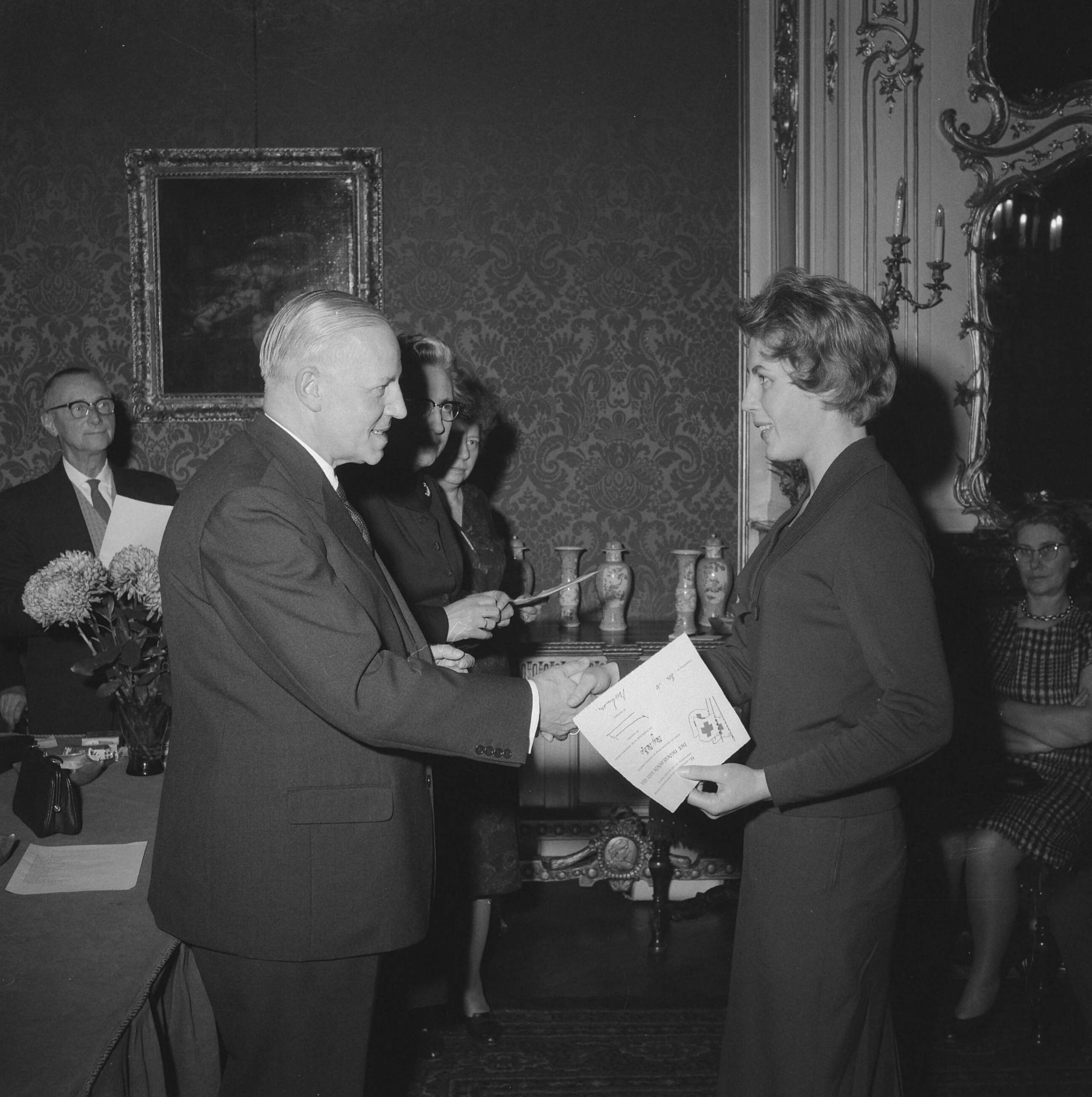 Fotocollectie Anefo — Uitreiking Rode Kruis campagnespeldjes te Den Haag. Notaris R. Remmelts, vice-voorzitter van de Haagse afdeling, reikt oorkonde uit — Foto: Behrens, Herbert F. / Anefo. Licentie: Set B: Rechtenvrij / Publiek Domein. Bron: Nationaal Archief. http://hdl.handle.net/10648/a9c225fc-d0b4-102d-bcf8-003048976d84