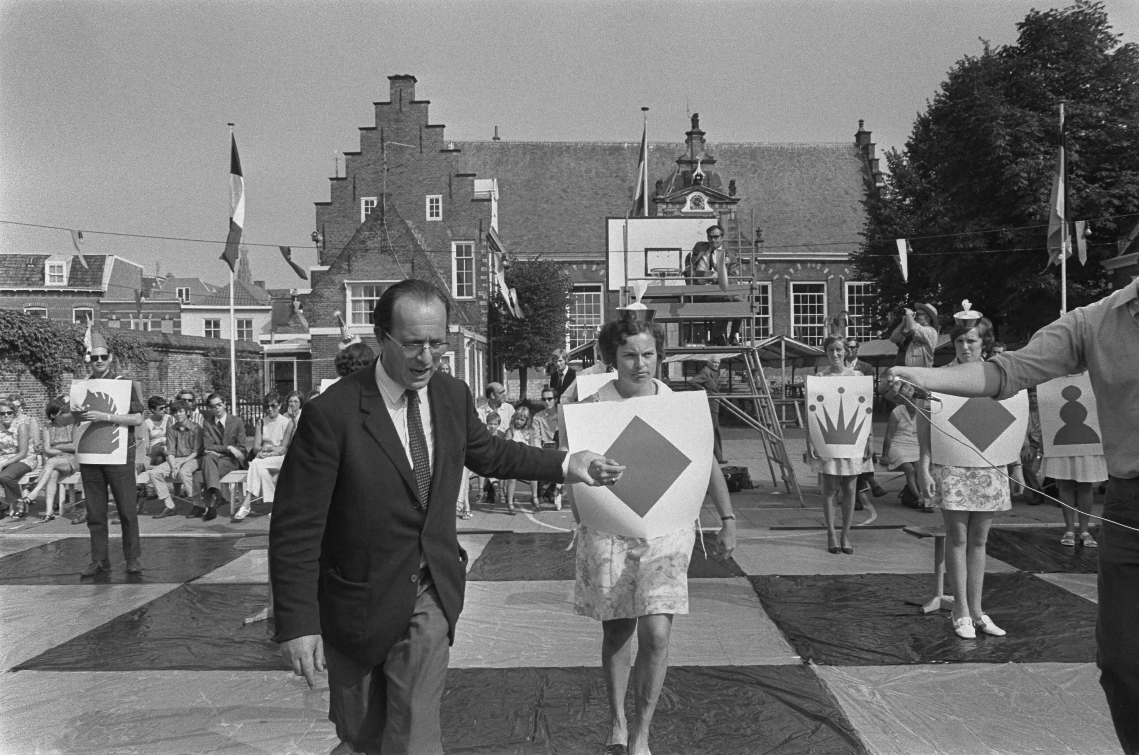 Fotocollectie Anefo — Godfried Bomans en dr. Max Euwe spelen schaakspel met levende stukken, Haarlem — Foto: Mieremet, Rob / Anefo. Licentie: Set B: Rechtenvrij / Publiek Domein. Bron: Nationaal Archief. http://hdl.handle.net/10648/aba13200-d0b4-102d-bcf8-003048976d84