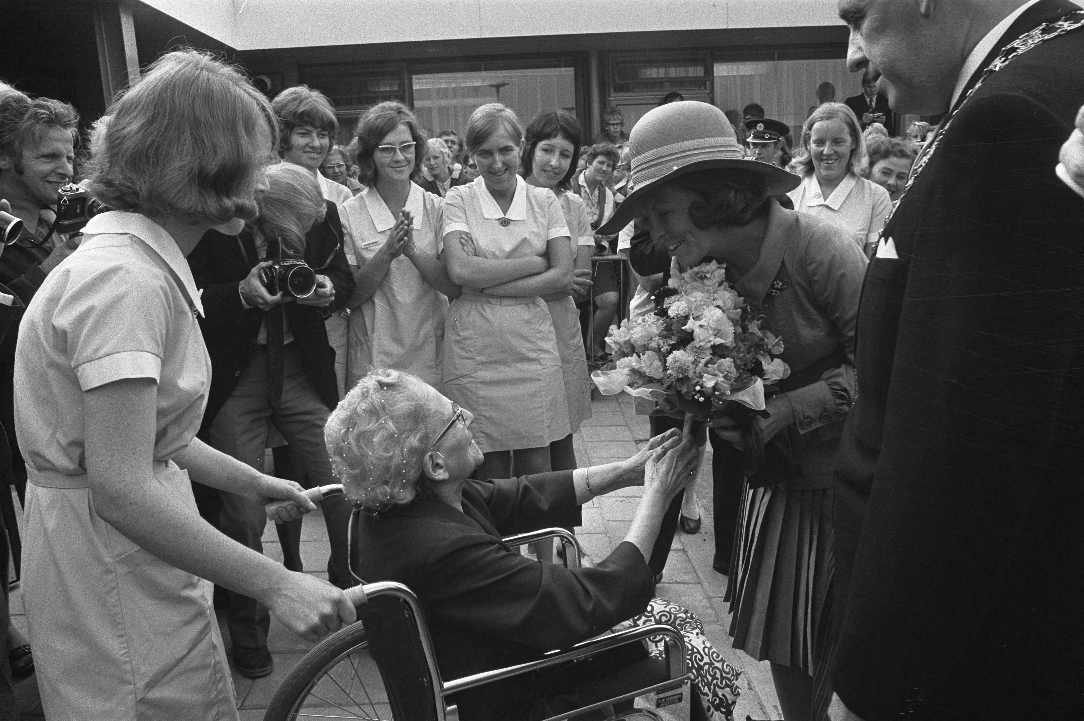 Fotocollectie Anefo — Prinses Beatrix opent ziekenhuiscomplex Triotel Leeuwarden, zij krijgt bloemen aangeboden door oudere vrouw in rolstoel — Foto: Verhoeff, Bert / Anefo. Licentie: Set B: Rechtenvrij / Publiek Domein. Bron: Nationaal Archief. http://hdl.handle.net/10648/abc9619e-d0b4-102d-bcf8-003048976d84