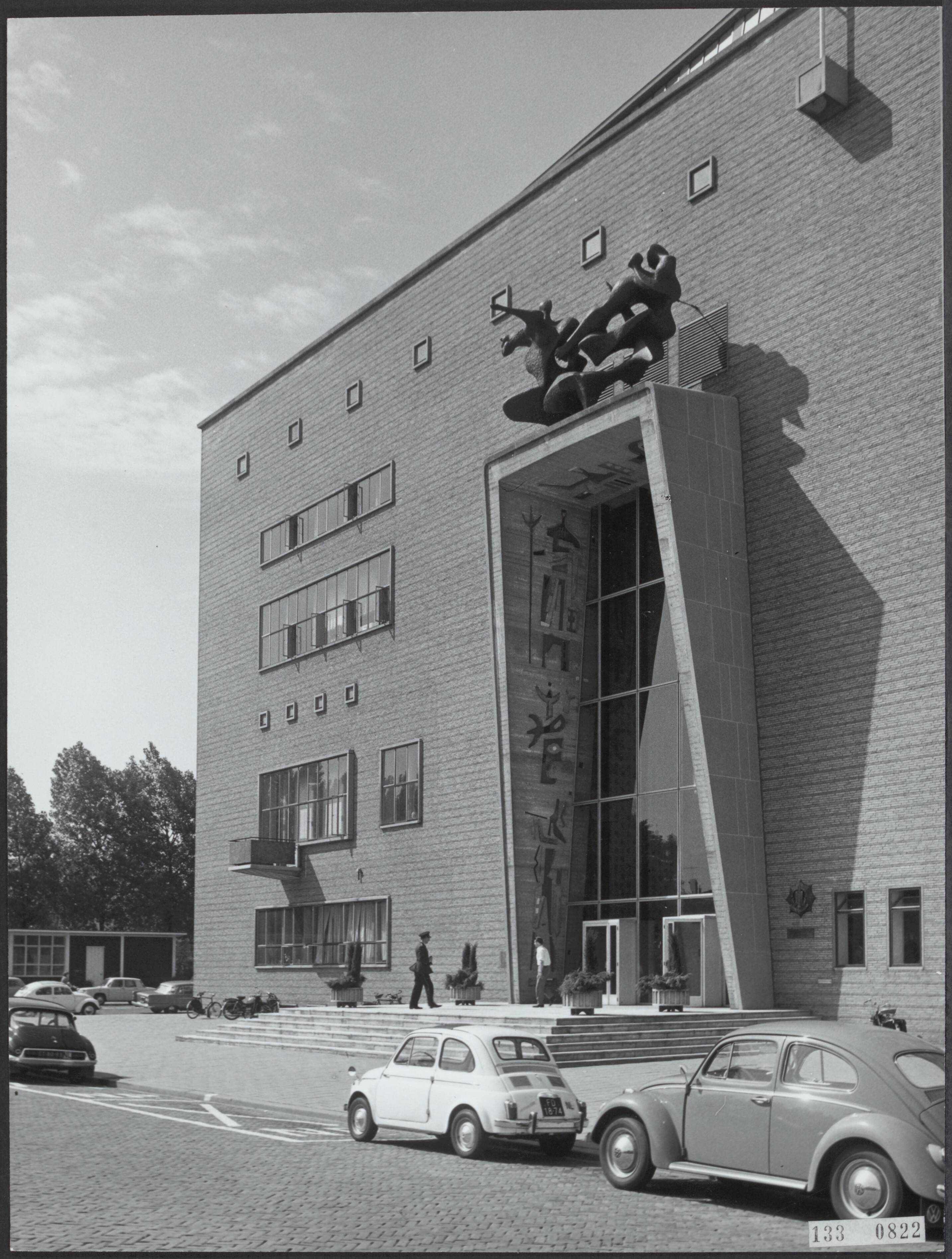 Fotocollectie Rijksvoorlichtingsdienst Eigen — Den Haag. Burgemeester De Monchyplein: hoofdbureau van politie met boven de ingang plastiek van Carel Kneulman (1915-2008) "Jacob en de engel" en tegen de binnenzijde van het portaal betonreliefs van O. Oxenaar (geb. 1929) — Foto: Fotodienst Gemeente Den Haag. Licentie: Set B: Rechtenvrij / Publiek Domein. Bron: Nationaal Archief. http://hdl.handle.net/10648/af5aa4bc-d0b4-102d-bcf8-003048976d84
