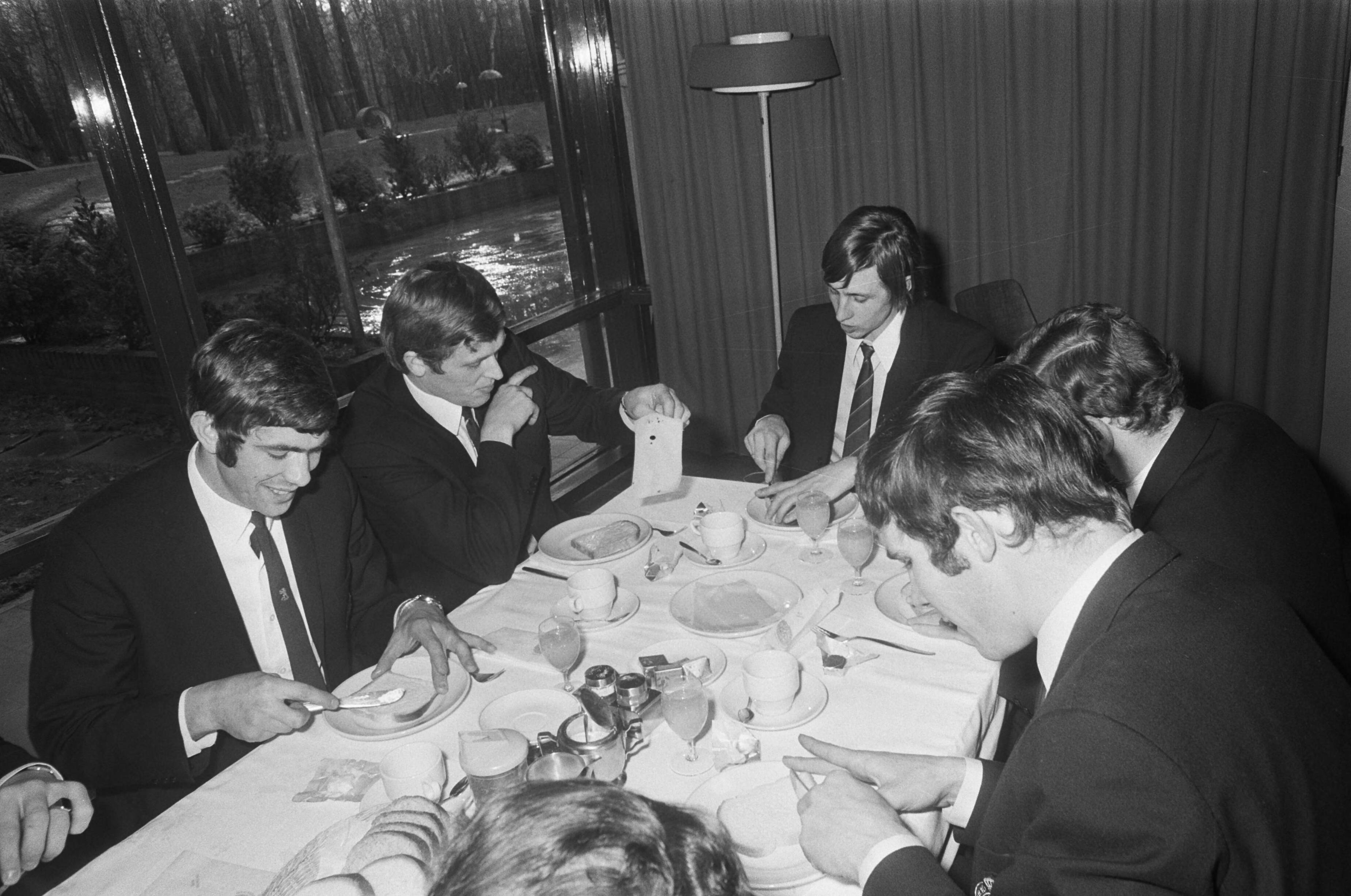 Fotocollectie Anefo — Nederlands elftal, dat tegen Engeland zal spelen in KNVB-sportcentrum te Zeist. Spelers aan lunch. Vlnr. Hans Eijkenbroek, Piet Keizer, Johan Cruijff, Wim Jansen, Willem van Hanegem — Foto: Mieremet, Rob / Anefo. Licentie: Set B: Rechtenvrij / Publiek Domein. Bron: Nationaal Archief. http://hdl.handle.net/10648/ab88aa32-d0b4-102d-bcf8-003048976d84