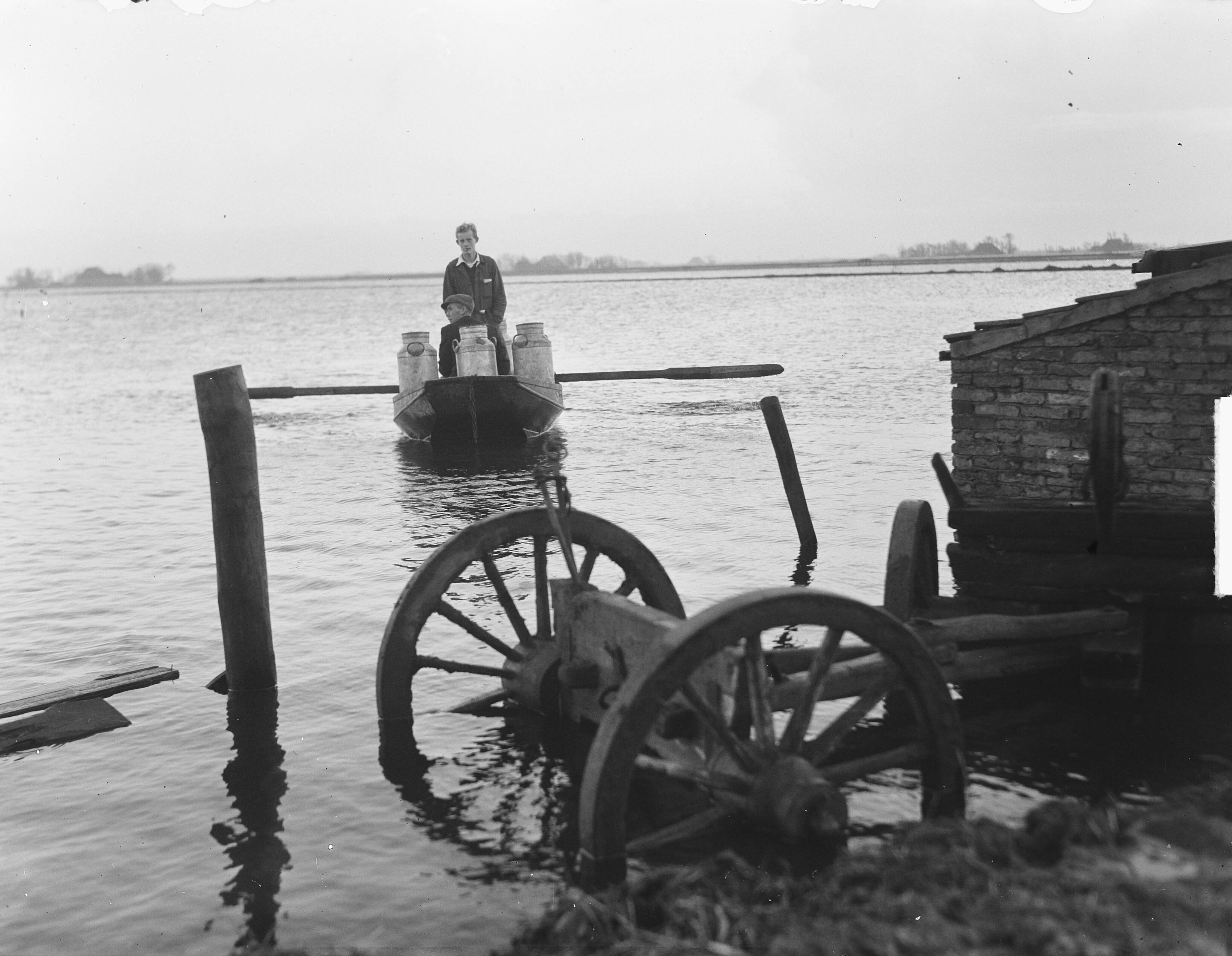 Hoogwater in Hempens (Friesland) — Hoog water in Friesland. Melkboer per vlot te Hempens — Foto: Oorschot, […] van / Anefo. Licentie: Set B: Rechtenvrij / Publiek Domein. Bron: Nationaal Archief. http://hdl.handle.net/10648/a8e50a46-d0b4-102d-bcf8-003048976d84