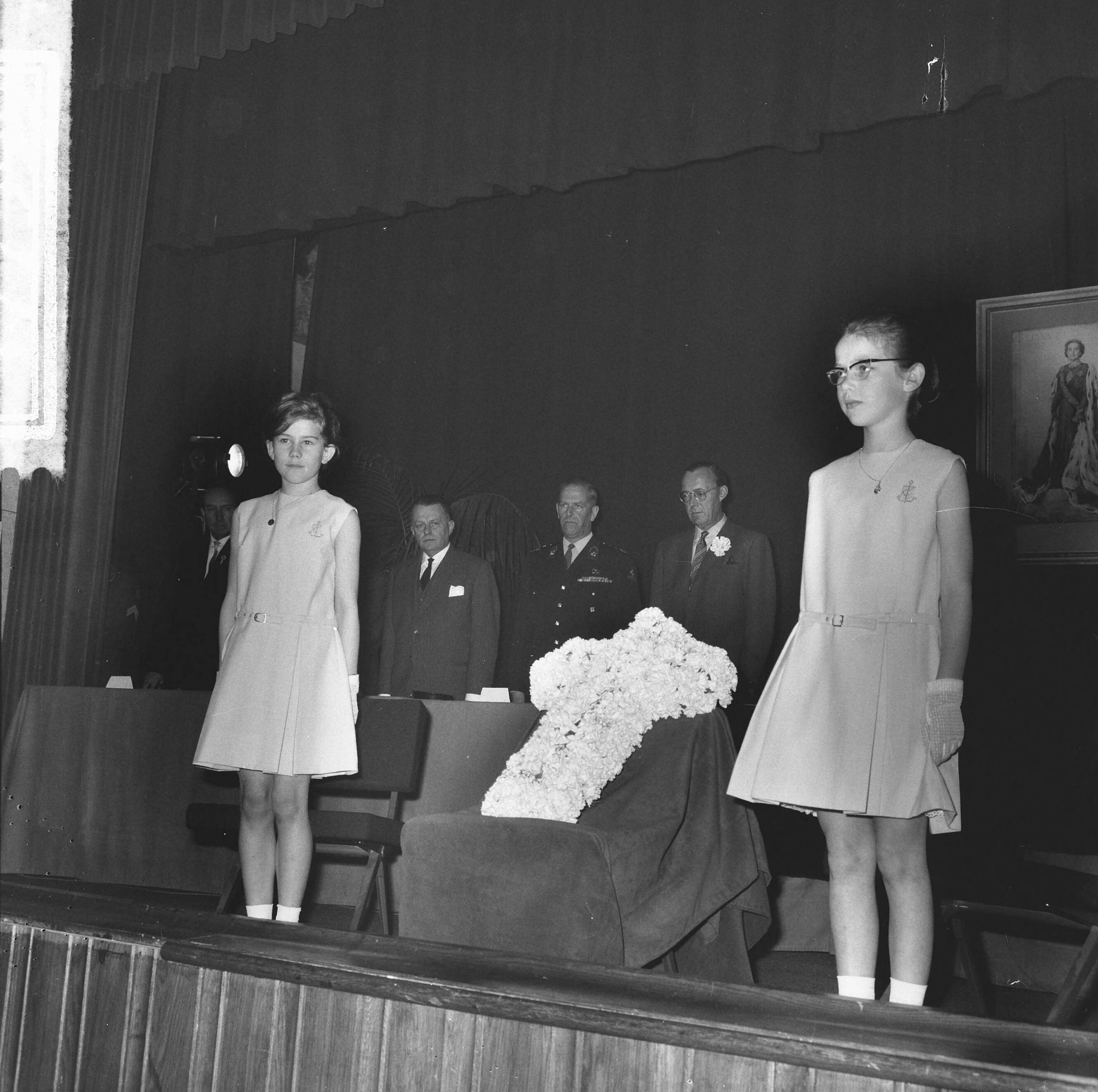 Fotocollectie Anefo — Bevrijdingscongres Nationale Federatie Raad van het Voormalig Verzet Nederland in de KMA te Breda, bijgewoond door prins Bernhard. Herdenking bij aanvang, twee meisjes plaatsen een kruis van witte anjers op een verhoging op het toneel — Foto: Nijs, Jac. de / Anefo. Licentie: Set B: Rechtenvrij / Publiek Domein. Bron: Nationaal Archief. http://hdl.handle.net/10648/aaa5c5e6-d0b4-102d-bcf8-003048976d84