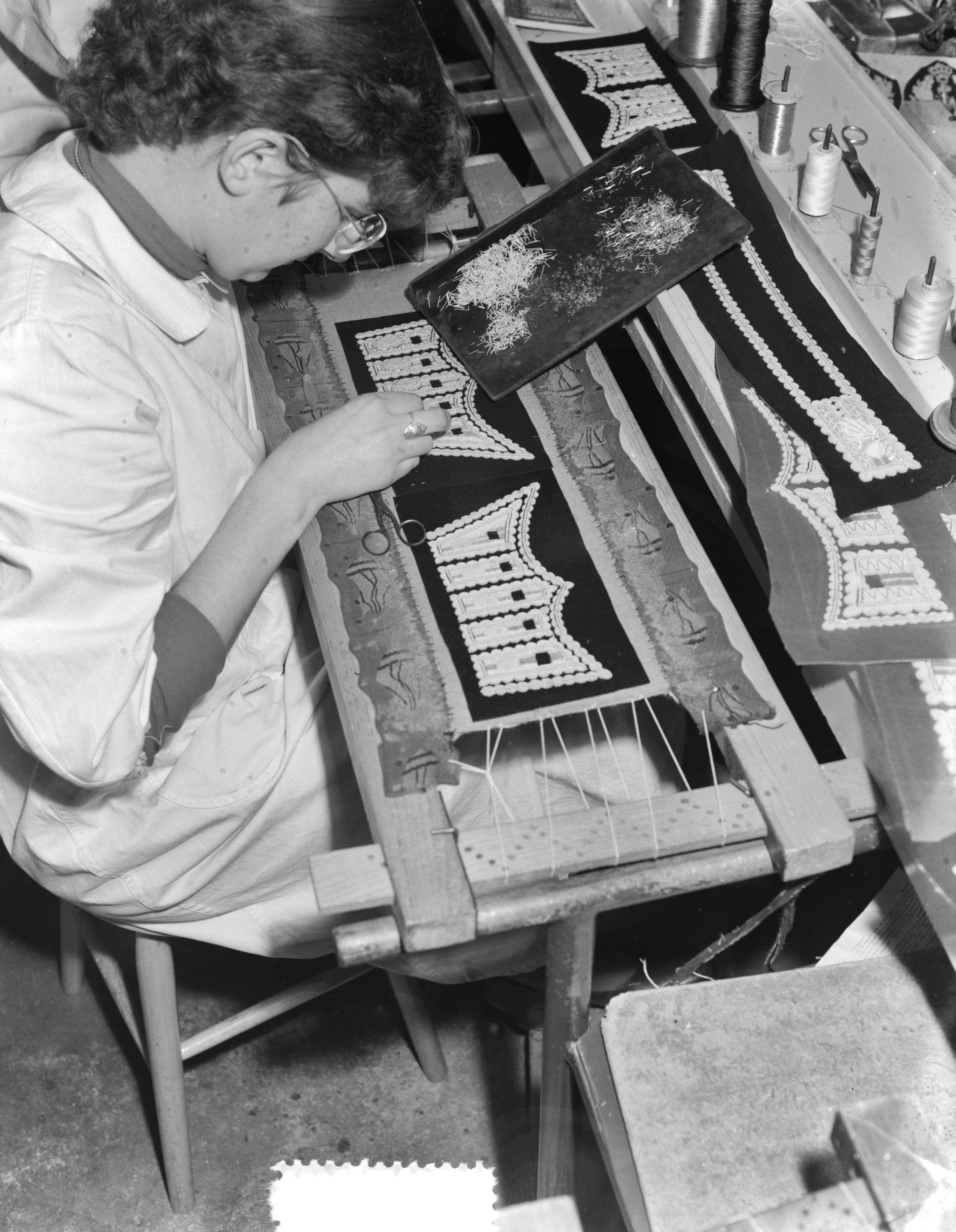 Fotocollectie Anefo — Bredase meisjes werken in Breda aan Engelse koningskleding. Het vervaardigen van borduursels voor de manchetsluitstukken voor de Welsh Guards — Foto: Duinen, G.W. van / Anefo. Licentie: Set B: Rechtenvrij / Publiek Domein. Bron: Nationaal Archief. http://hdl.handle.net/10648/a9054c98-d0b4-102d-bcf8-003048976d84