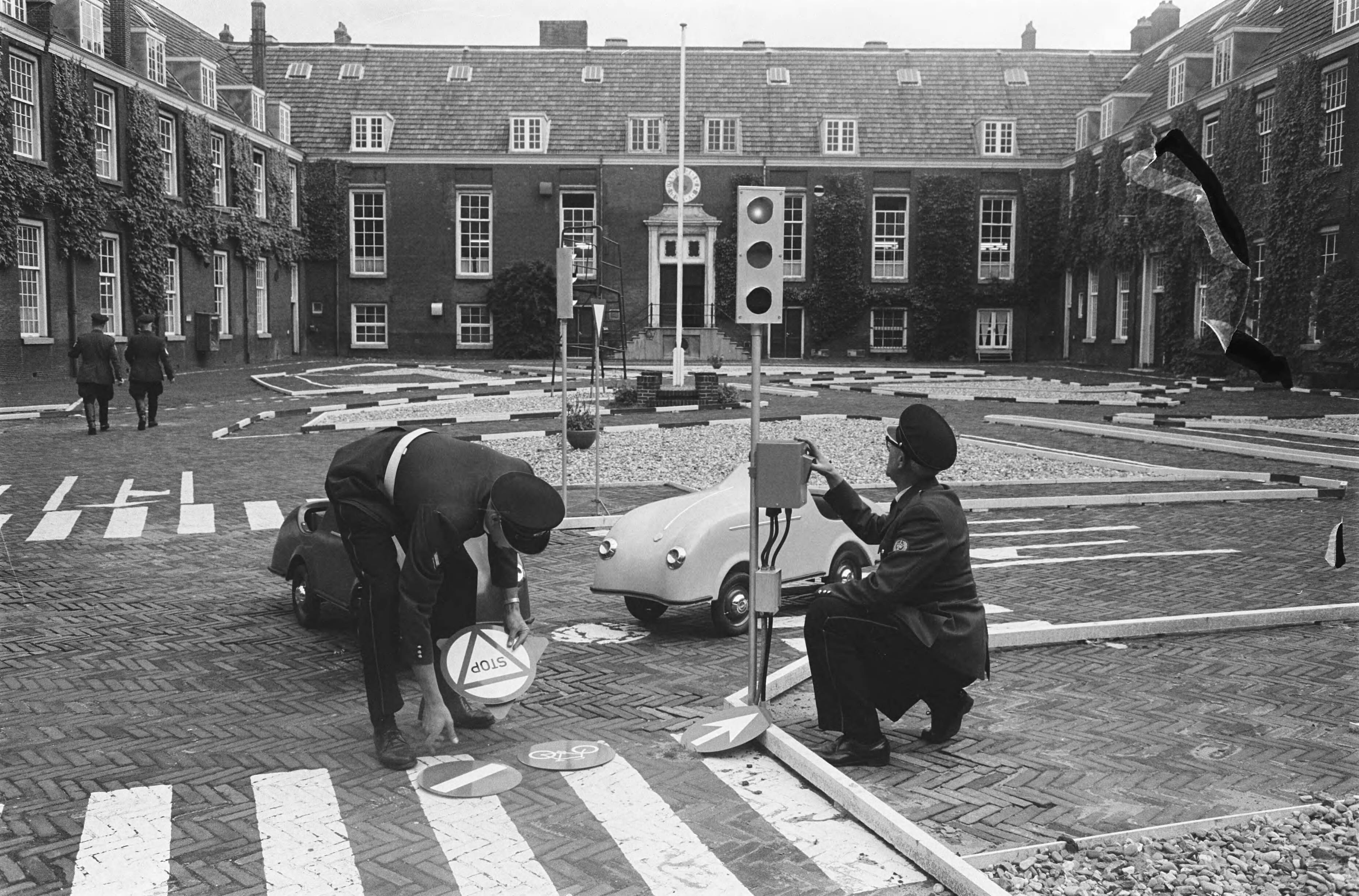 Fotocollectie Anefo — In Koudehornkazerne te Haarlem heeft de Haarlemse verkeerspolitie een verkeerstuin ingericht. Brigadier P. van Deenen en assisten-agent Van Hurk leggen de laatste hand aan de verkeerstuin, die volgens plan in september geopend wordt — Foto: Pot, Harry / Anefo. Licentie: Set B: Rechtenvrij / Publiek Domein. Bron: Nationaal Archief. http://hdl.handle.net/10648/aa4343da-d0b4-102d-bcf8-003048976d84