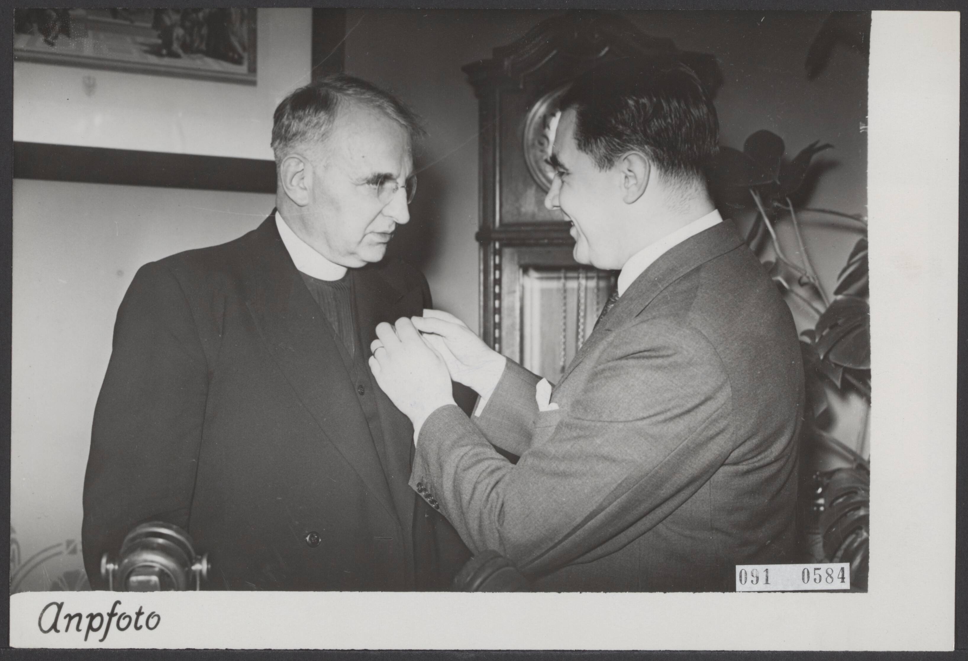 Fotocollectie Elsevier Binnenland — Pater Henri de Greeve, als radiospreker en stichter van de Bond zonder Naam een bekende figuur, herdacht het feit dat hij 25 jaar geleden tot priester werd gewijd. In het ziekenhuis Joannes de Deo te Haarlem werd hem hulde gebracht voor zijn sociale arbeid. Minister mr. E.M.J.A. Sassen, die als vriend van de jubilaris aanwezig was, deed mededeling van zijn benoeming tot officier in de orde van Oranje Nassau en speldde hem de onderscheiding op de borst — Foto: ANP / RVD of rechtenvrij. Licentie: Set B: Rechtenvrij / Publiek Domein. Bron: Nationaal Archief. http://hdl.handle.net/10648/ae206654-d0b4-102d-bcf8-003048976d84