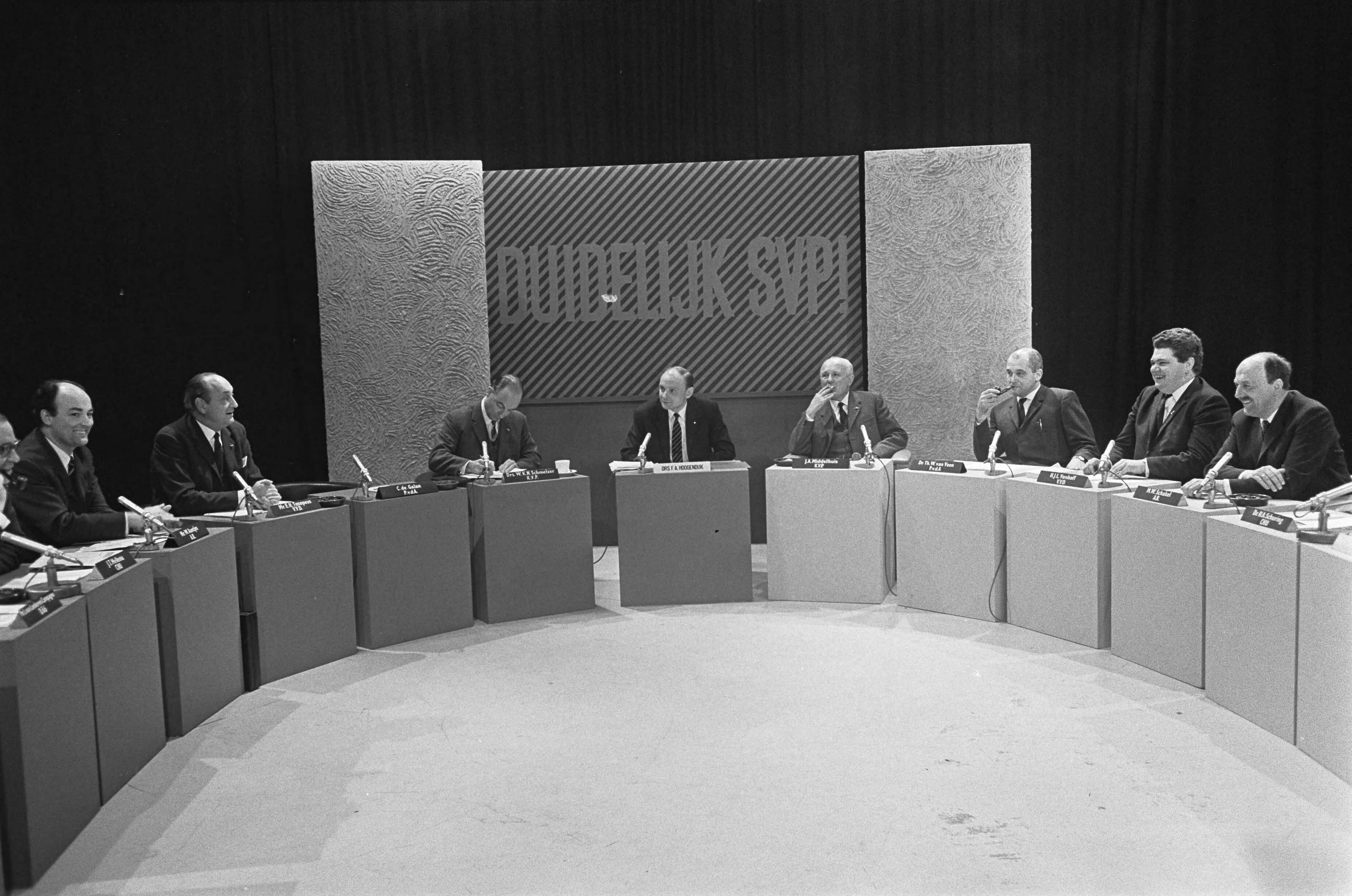 Fotocollectie Anefo — AVRO-TV, "Duidelijk svp" , zestien Nederlandse politici debatteren onder leiding van drs. F. A. Hoogendijk (midden) — Foto: Koch, Eric / Anefo. Licentie: Set B: Rechtenvrij / Publiek Domein. Bron: Nationaal Archief. http://hdl.handle.net/10648/ab34dd80-d0b4-102d-bcf8-003048976d84