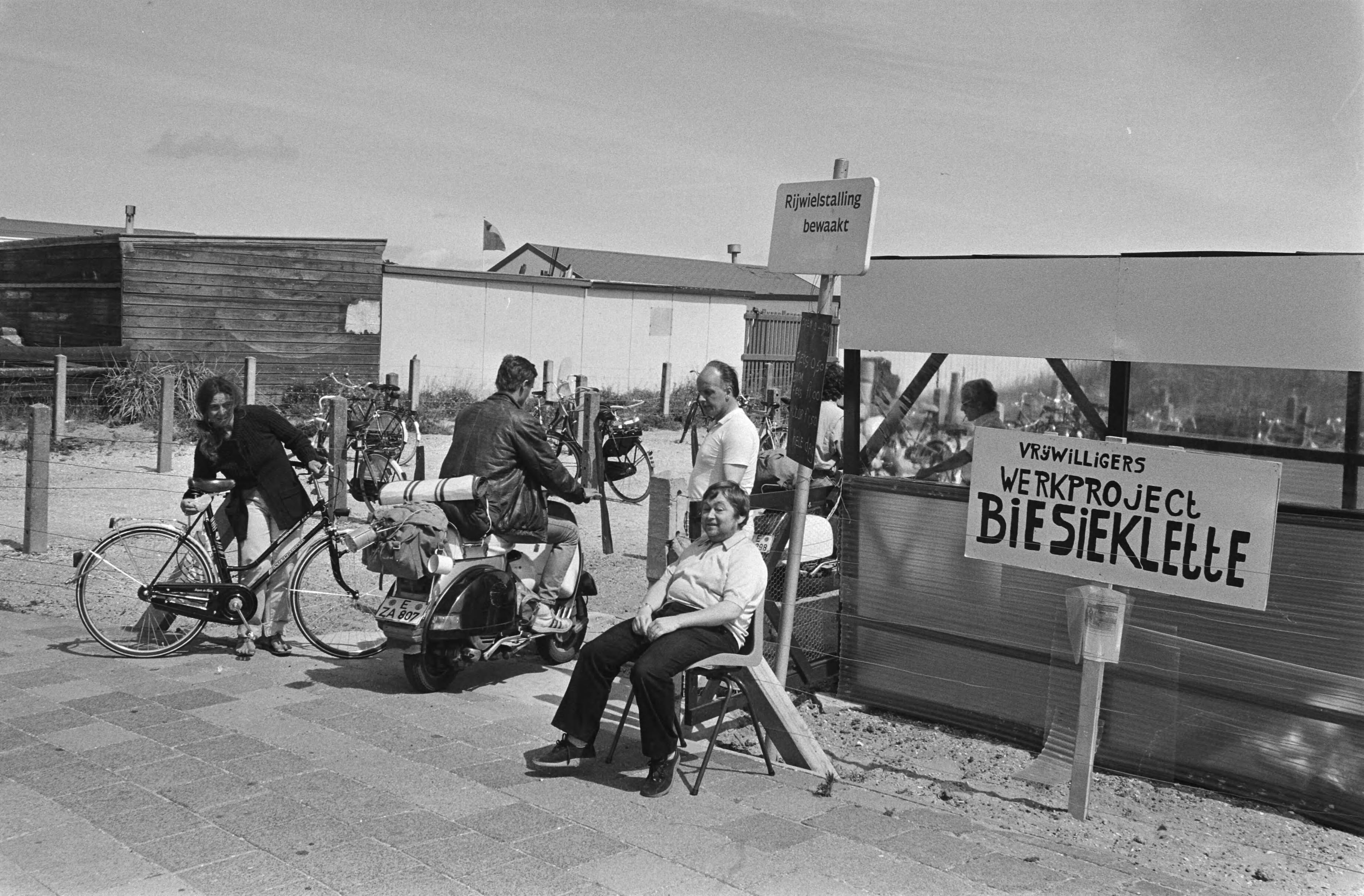 Fietsenstalling bemand door werklozen, met behoud van uitkering in Scheveningen — Medewerkers bij een bord "Vrijwilligers werkproject Biesieklette" — Foto: Antonisse, Marcel / Anefo. Licentie: Set B: Rechtenvrij / Publiek Domein. Bron: Nationaal Archief. http://hdl.handle.net/10648/ad2be7f0-d0b4-102d-bcf8-003048976d84