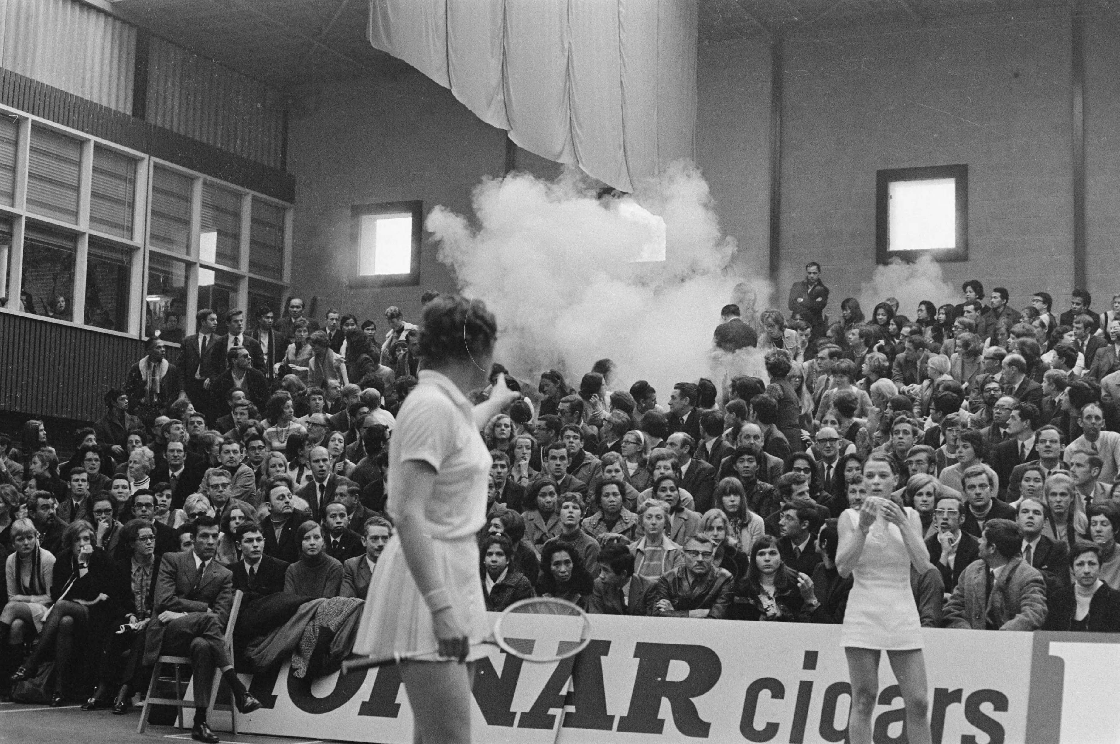 Fotocollectie Anefo — Internationale badmintonwedstrijden in Duinwijckhal Haarlem Mejuffrouw Whetnall wijst waar rookbom is gevallen, rechts mejuffrouw Bostofte (Denen) / — Foto: Verhoeff, Bert / Anefo. Licentie: Set B: Rechtenvrij / Publiek Domein. Bron: Nationaal Archief. http://hdl.handle.net/10648/ab8d4268-d0b4-102d-bcf8-003048976d84
