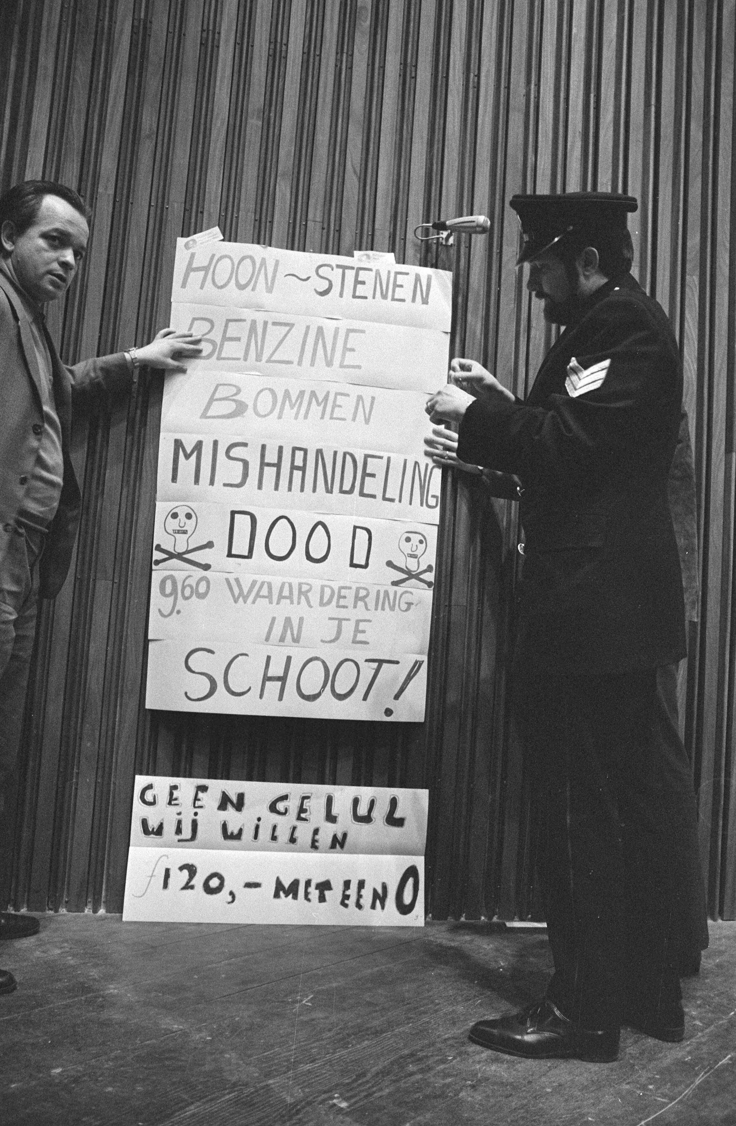 Fotocollectie Anefo — Protestvergadering van 2.000 politiemannen in Congresgebouw Den Haag ; o.a. voor betere salariering agent hangt borden op — Foto: Verhoeff, Bert / Anefo. Licentie: Set B: Rechtenvrij / Publiek Domein. Bron: Nationaal Archief. http://hdl.handle.net/10648/abac5554-d0b4-102d-bcf8-003048976d84