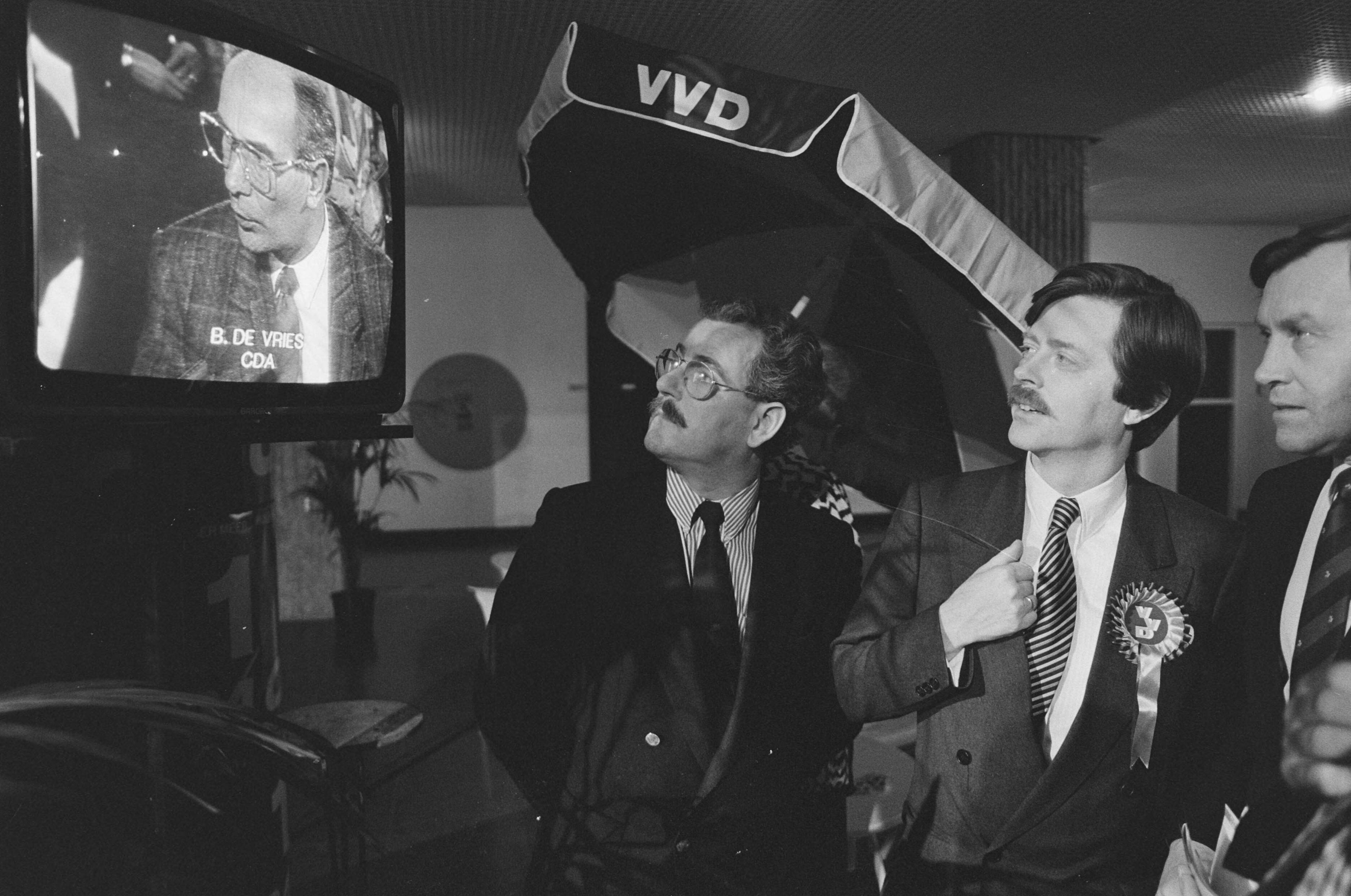 Fotocollectie Anefo — Provinciale Statenverkiezingen 1987; VVD-leider Voorhoeve (r) kijkt naar CDA-collega De Vries op tv in Den Haag — Foto: Croes, Rob C. / Anefo. Licentie: Set B: Rechtenvrij / Publiek Domein. Bron: Nationaal Archief. http://hdl.handle.net/10648/ad5e0794-d0b4-102d-bcf8-003048976d84