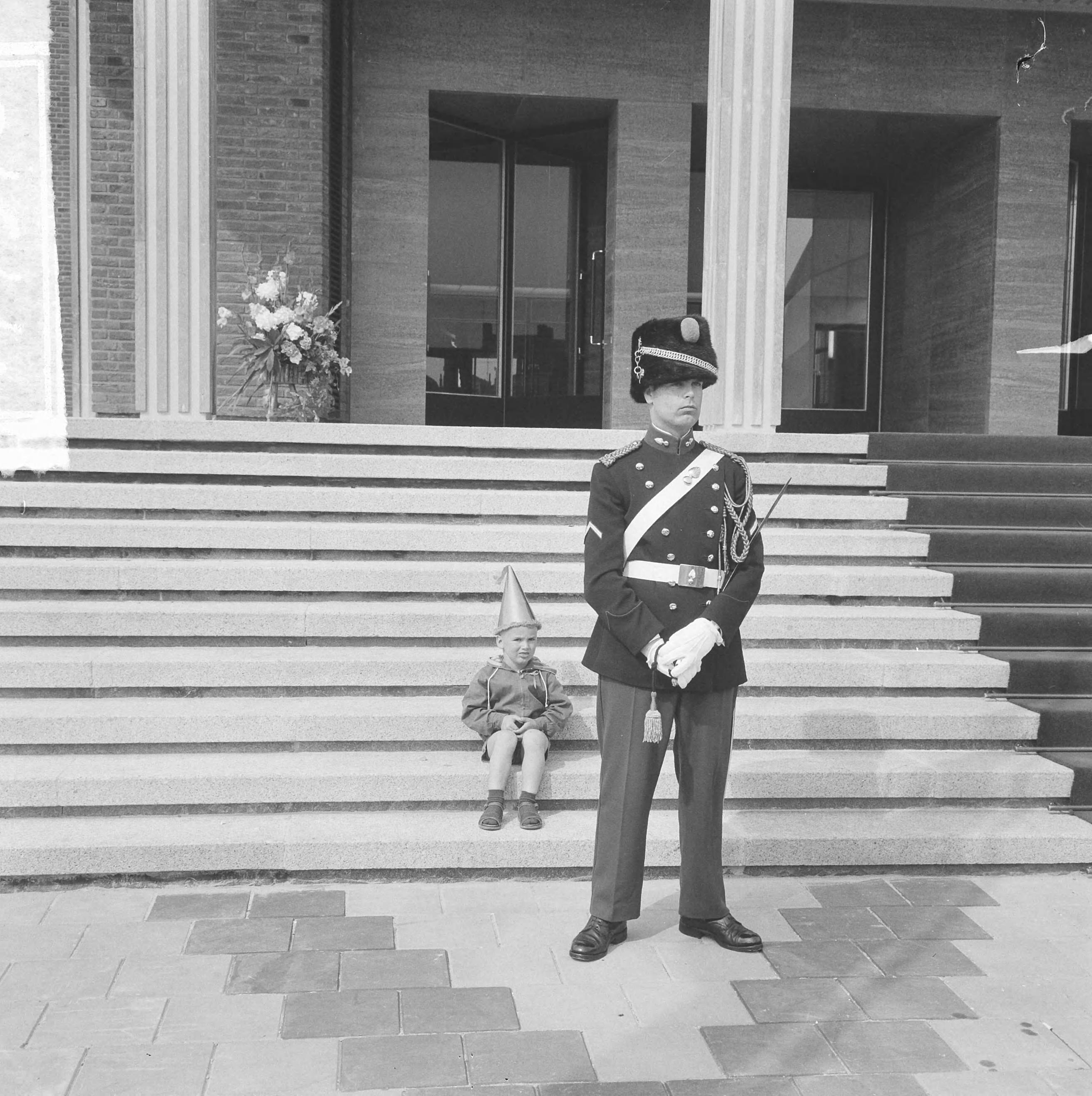 Koningin Juliana opent het nieuwe stadhuis te Vlissingen — Een jongetje met feestmuts zit op de trappen van het bordes. Voor hem staat een marechaussee — Foto: Nijs, Jac. de / Anefo. Licentie: Set B: Rechtenvrij / Publiek Domein. Bron: Nationaal Archief. http://hdl.handle.net/10648/422f231c-dcc0-6692-ad79-cfe3541acfa6