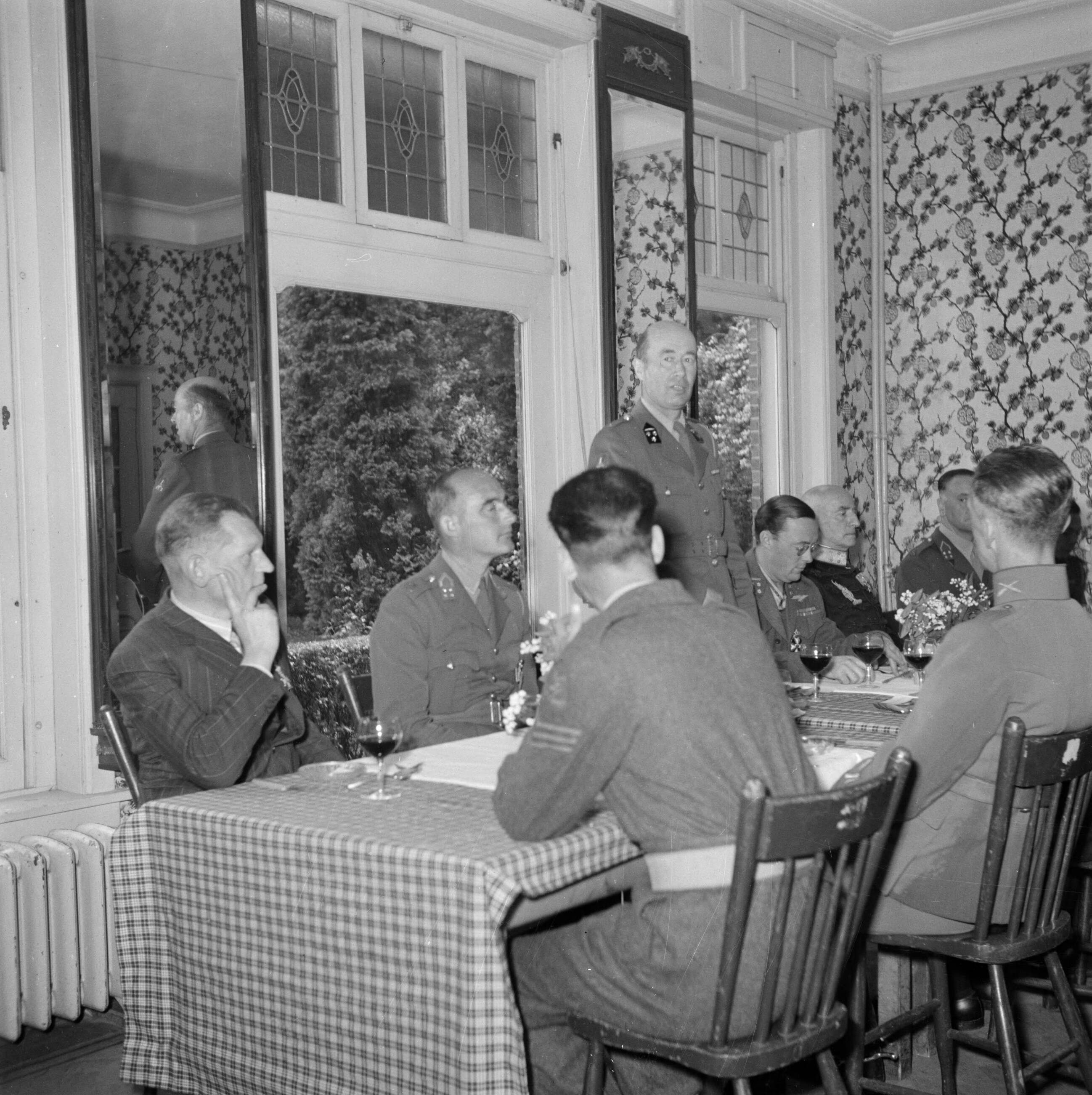 Uitreiking van de Militaire Willems-Orde en andere onderscheidingen door koningin Wilhelmina in aanwezigheid van de overige leden van de koninklijke familie op de vliegbasis Soesterberg — Gedecoreerden en genodigden luisterend naar een tafelspeech, met rechts van de spreker prins Bernhard — Foto: Poll, Willem van de. Licentie: Set B: Rechtenvrij / Publiek Domein. Bron: Nationaal Archief. http://hdl.handle.net/10648/aee908ca-d0b4-102d-bcf8-003048976d84