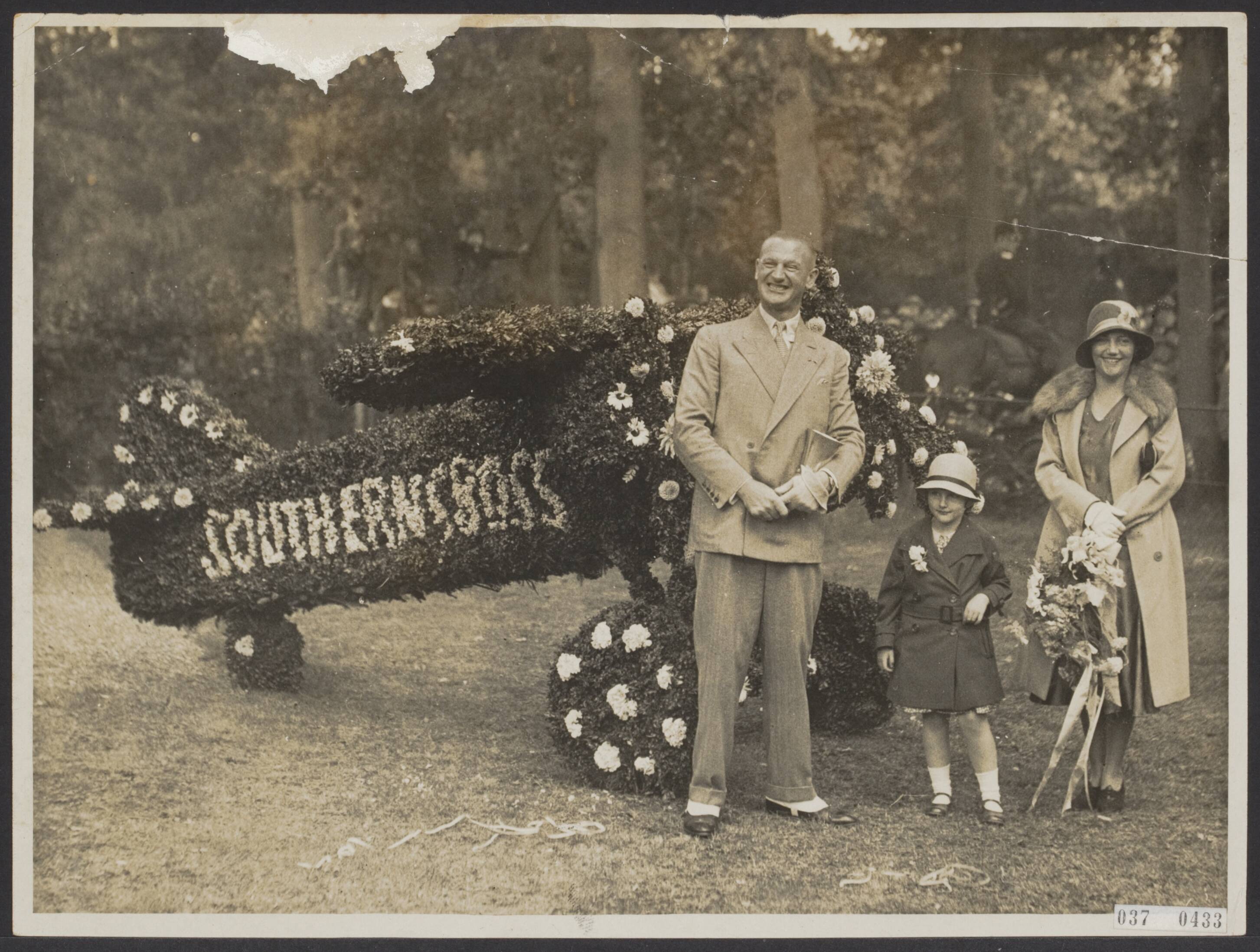 Fotocollectie Elsevier Binnenland — Bijschrift foto: "Evert van Dijk gehuldigd. In de tuin van zijn villa was van groen en bloemen een vliegmachine opgesteld. Iet s dat door van Dijk zeer op prijs werd gesteld". [Huldiging door het gemeentebestuur Wassenaar n.a.v. de vlucht van Ierland naar Newfoundland, en later New York, met de Fokker VIIb "Southern Cross". Co-piloot Evert van Dijk met gezin] — Foto: N.V. Polygoon. Licentie: Set B: Rechtenvrij / Publiek Domein. Bron: Nationaal Archief. http://hdl.handle.net/10648/adeed850-d0b4-102d-bcf8-003048976d84
