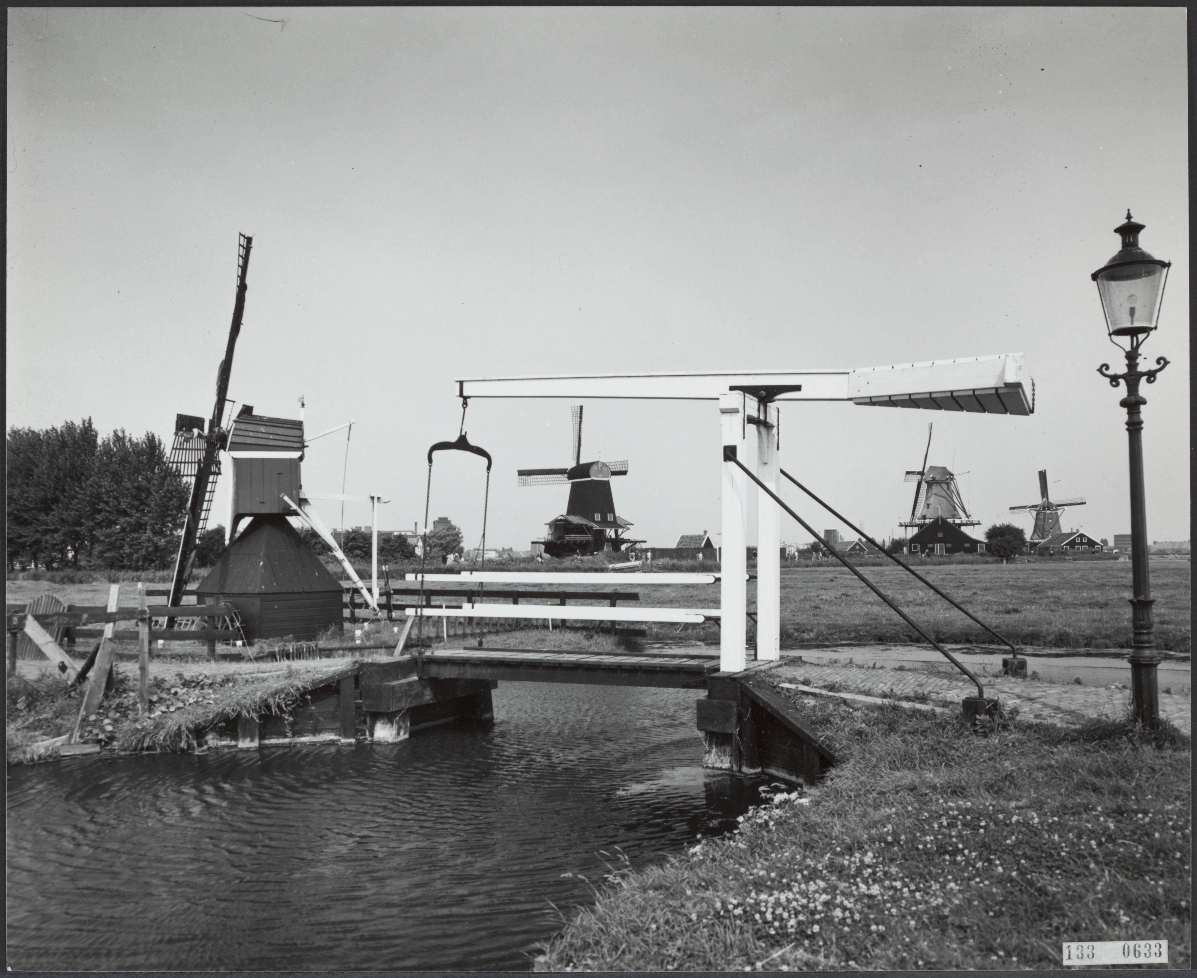 Fotocollectie Rijksvoorlichtingsdienst Eigen — Zaanstad. Openluchtmuseum Zaanse Schans te Zaandam. Van links naar rechts: gedeeltelijk zichtbaar wipmolen De Hadel, paltrokmolen De Gekroonde Poelenburg, Verfmolen De Kat en oliemolen De Zoeker. Op de voorgrond een ophaalbrug — Foto: Publicam / Hartemink, Piet. Licentie: Set B: Rechtenvrij / Publiek Domein. Bron: Nationaal Archief. http://hdl.handle.net/10648/af59e004-d0b4-102d-bcf8-003048976d84