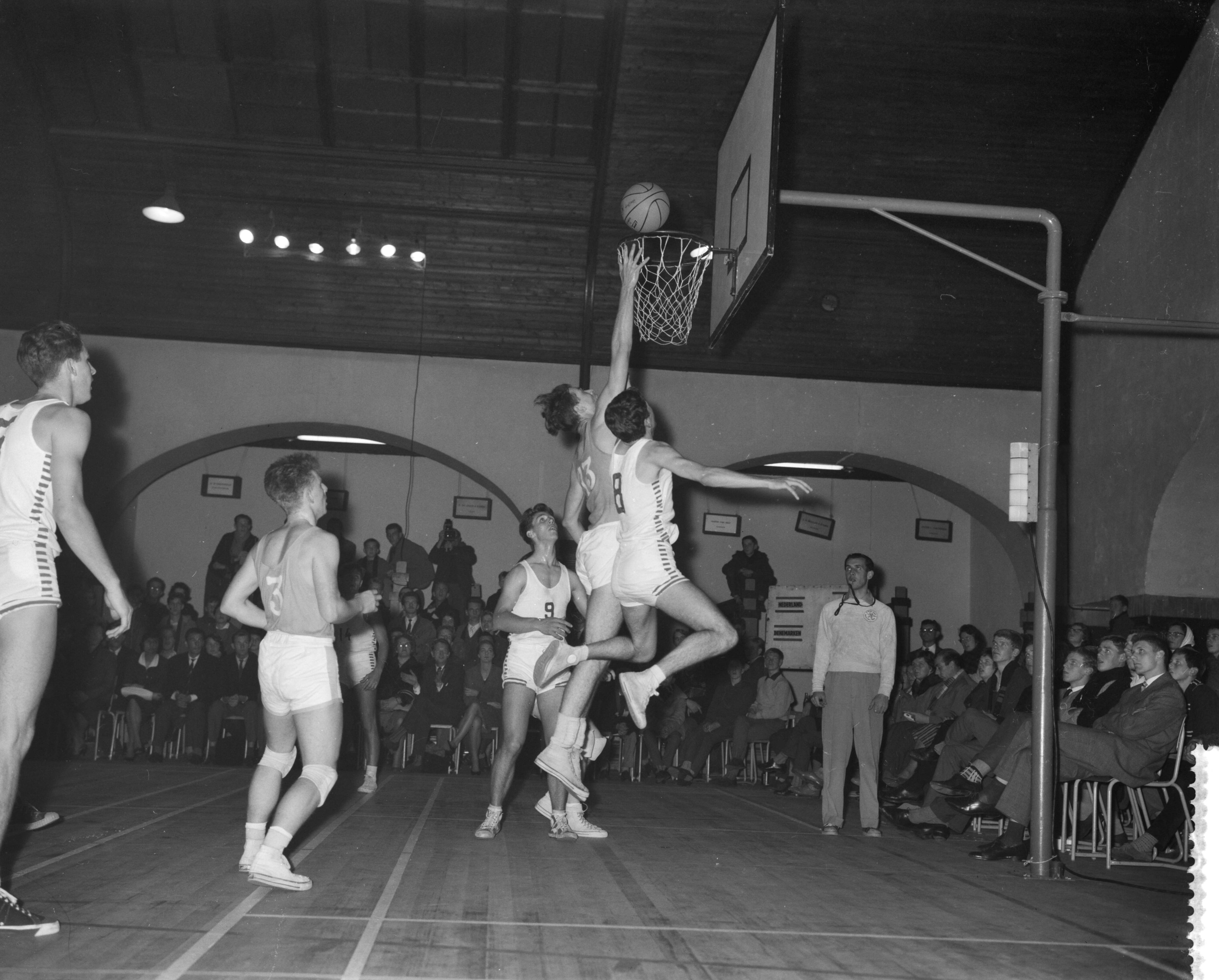 Fotocollectie Anefo — Basketbalwedstrijd Nederland tegen Denemarken in het Krelage Huis te Haarlem (70-54). Sleeswijk (midden) scoort, links Fleming Wick en rechts Per Nielsen — Foto: Rossem, Wim van / Anefo. Licentie: Set B: Rechtenvrij / Publiek Domein. Bron: Nationaal Archief. http://hdl.handle.net/10648/a9bd84ca-d0b4-102d-bcf8-003048976d84