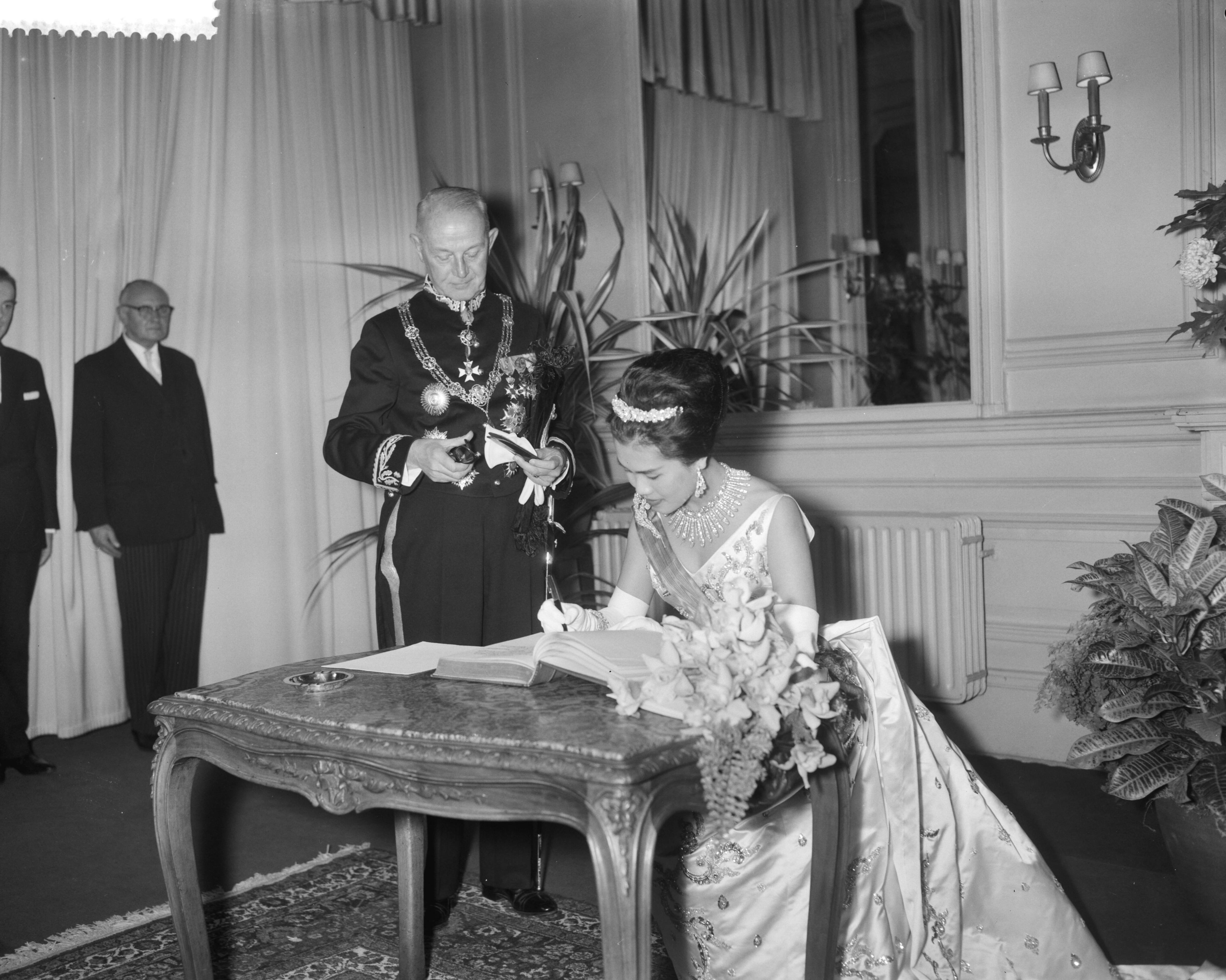 Fotocollectie Anefo — Galaconcert door Koninklijke Militaire Kapel in de Kurzaal te Den Haag , Koningin Sirikit tekent gastenboek, links burgemeester Kolfschoten — Foto: Bilsen, Joop van / Anefo. Licentie: Set B: Rechtenvrij / Publiek Domein. Bron: Nationaal Archief. http://hdl.handle.net/10648/a9bca334-d0b4-102d-bcf8-003048976d84