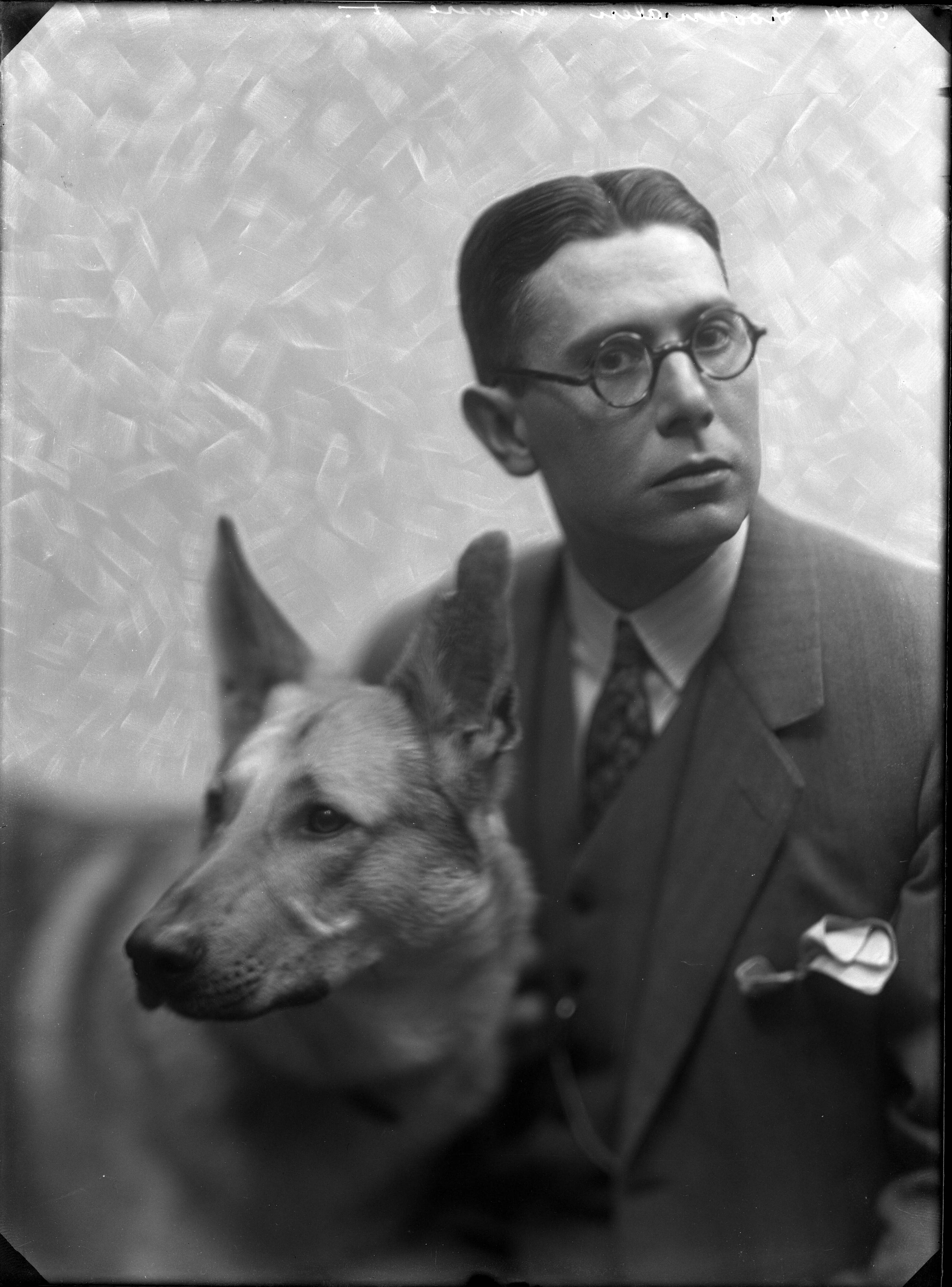 Portretten — Studio-opnames. Portret van een man in driedelig pak met donkere ronde bril samen met zijn herdershond. Haarlem, Nederland. 1918-1930. 9241 Roozemalen gravure [t.] — Foto: Berg, Th.C.J. van den / Spaarnestad Photo (05887). Licentie: Set B: Rechtenvrij / Publiek Domein. Bron: Nationaal Archief. http://hdl.handle.net/10648/35429da7-c76a-a382-e063-6df0900a6686