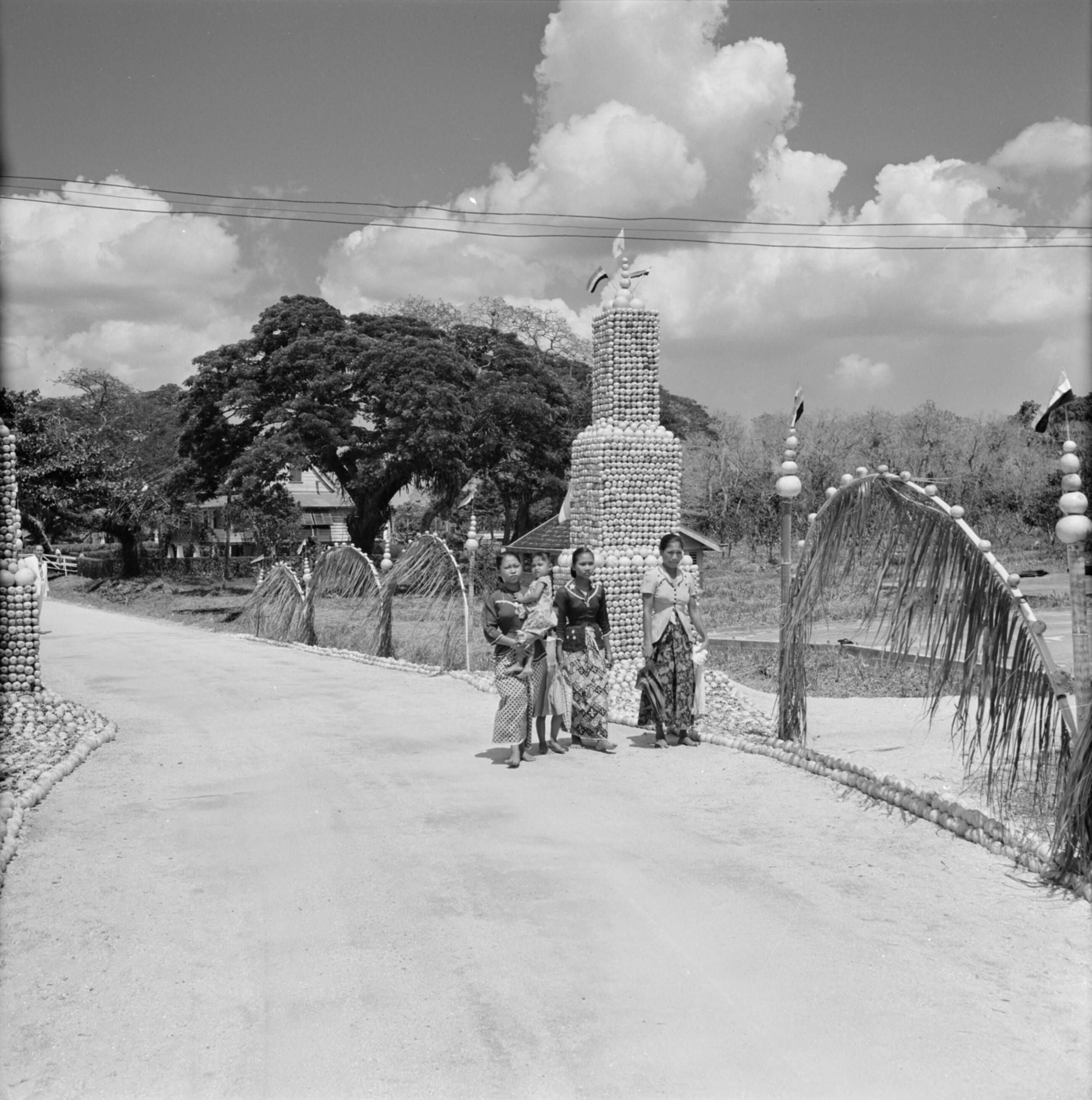 Nederlandse Antillen en Suriname ten tijde van het koninklijk bezoek van koningin Juliana en prins Bernhard in 1955 — Javaanse vrouwen voor een toren van citrusvruchten in Voorburg — Foto: Poll, Willem van de. Licentie: Set B: Rechtenvrij / Publiek Domein. Bron: Nationaal Archief. http://hdl.handle.net/10648/aeb37a52-d0b4-102d-bcf8-003048976d84