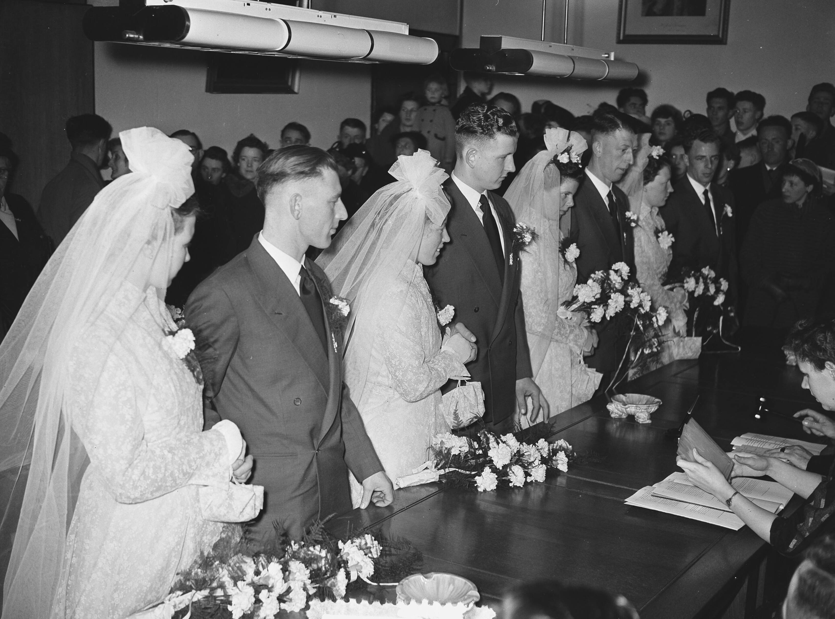 Fotocollectie Anefo — Meervoudige bruiloft. Op het gemeentehuis van Leimuiden trouwden vier telgen uit het gezin Brand (15 kinderen) tegelijkertijd. Vlnr. Het zijn van links naar rechts: Toon Brand (28 jaar, chauffeur) en Catharina Lemmens, Nellie Brand (23 jaar) en Theo Obdam (timmerman), Bram Brand (26 jaar, metselaar) en Bep Könst, en Dora Brand (24 jaar) en Kees Könst (bloemist) — Foto: Pot, Harry / Anefo. Licentie: Set B: Rechtenvrij / Publiek Domein. Bron: Nationaal Archief. http://hdl.handle.net/10648/a930c904-d0b4-102d-bcf8-003048976d84