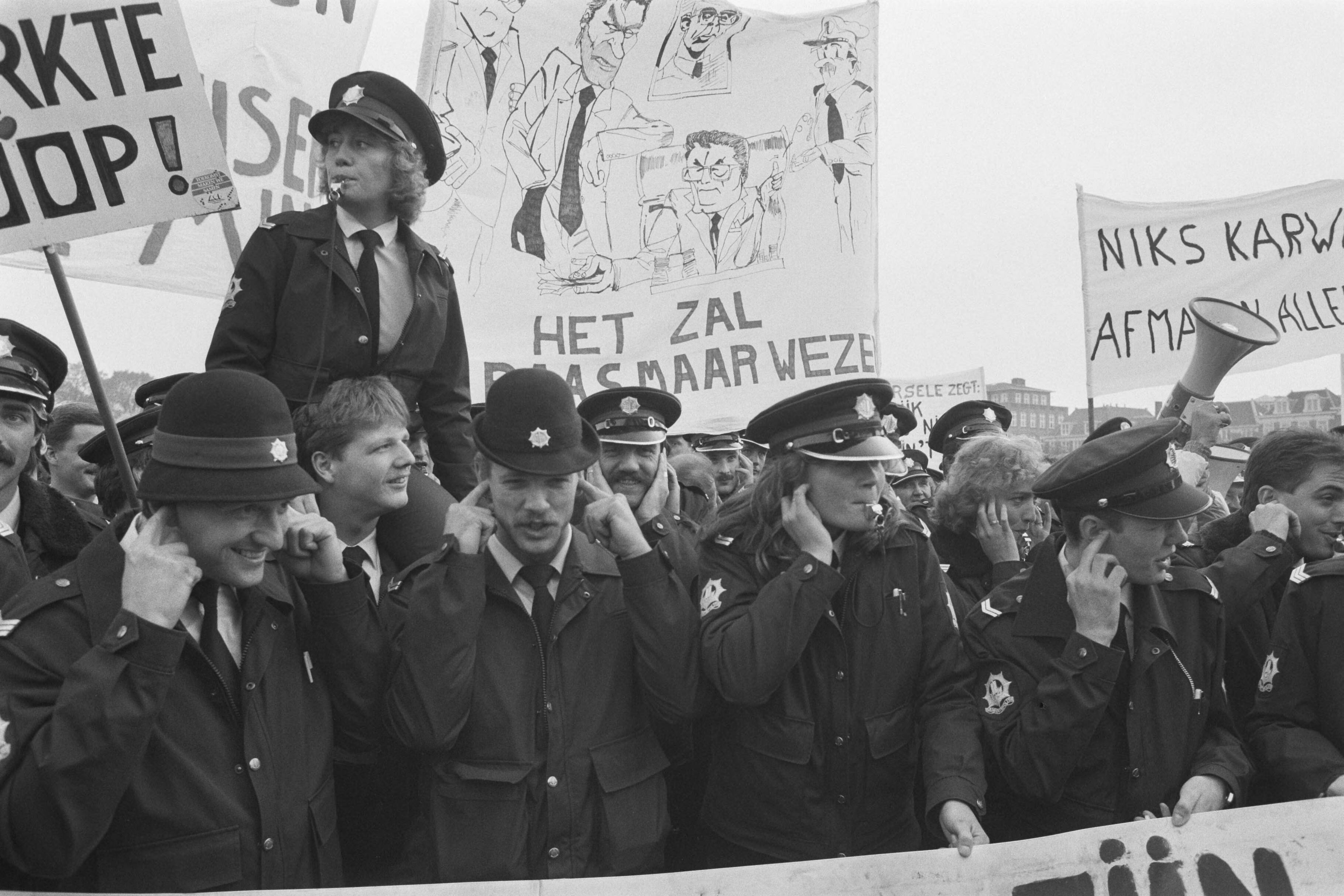 Fotocollectie Anefo — Politie demonstreert in Den Haag tegen bezuinigingen; politievrouw op schouders mannelijke collegas — Foto: Croes, Rob C. / Anefo. Licentie: Set B: Rechtenvrij / Publiek Domein. Bron: Nationaal Archief. http://hdl.handle.net/10648/ad657588-d0b4-102d-bcf8-003048976d84
