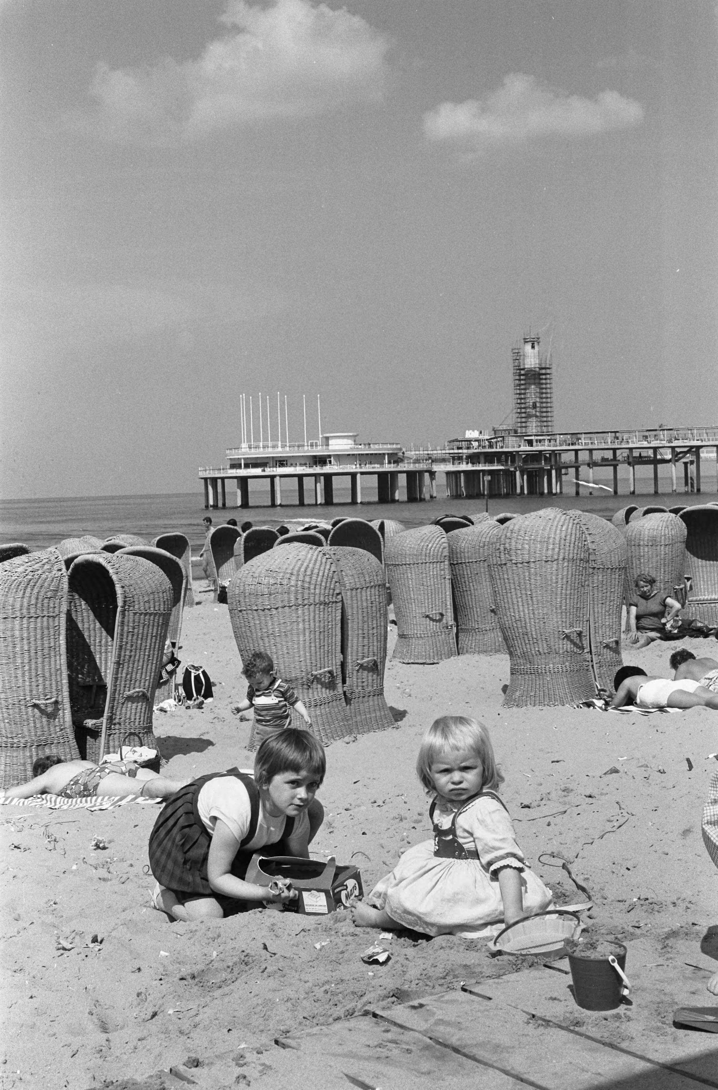 Fotocollectie Anefo — De nieuwe Pier in Scheveningen. Strandbeeld met in de achtergrond de nieuwe pier in aanbouw — Foto: Pot, Harry / Anefo. Licentie: Set B: Rechtenvrij / Publiek Domein. Bron: Nationaal Archief. http://hdl.handle.net/10648/a9d2e4dc-d0b4-102d-bcf8-003048976d84
