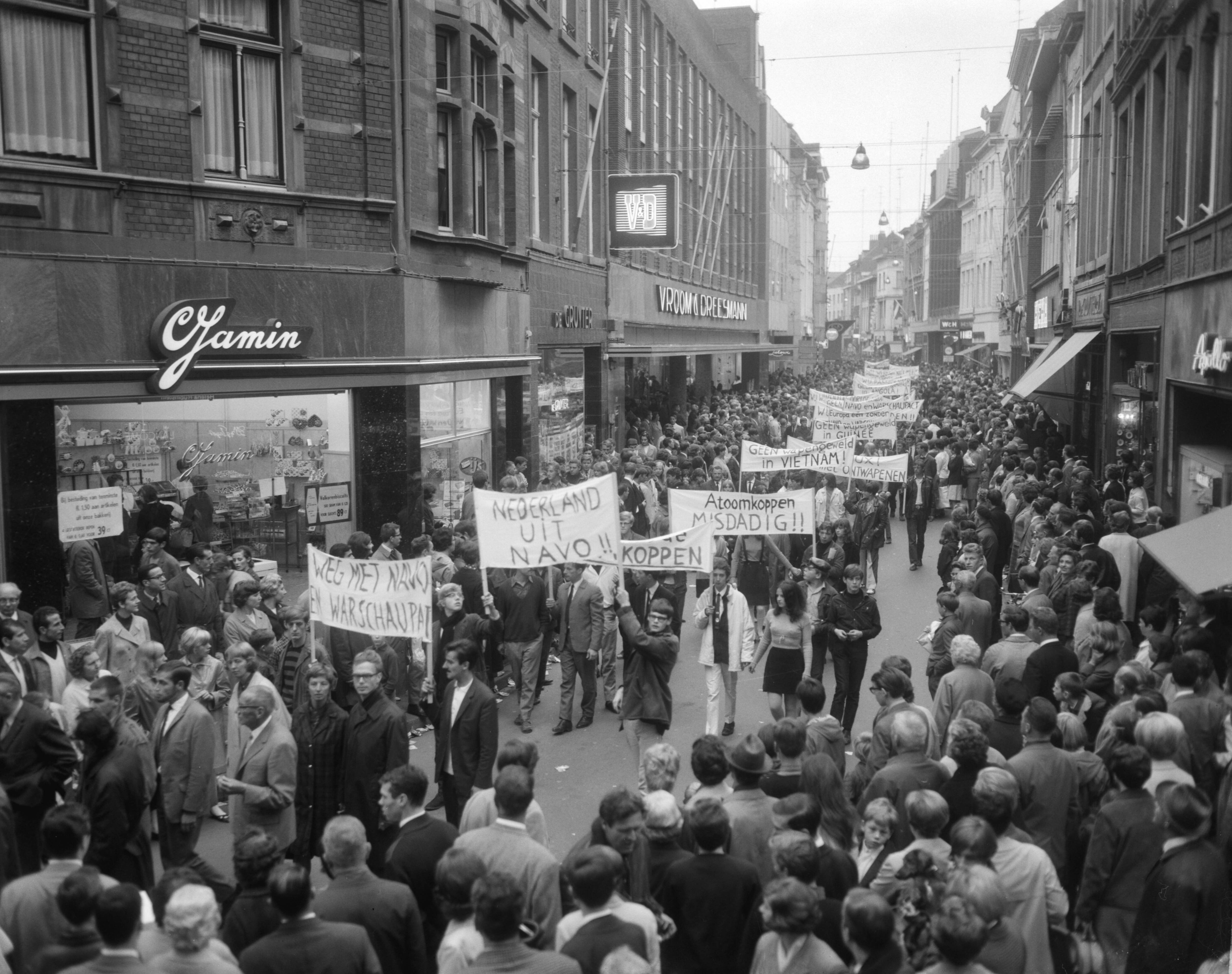 Anti NAVO-demonstratie in Maastricht — Demonstranten met spandoeken in de Grote Straat — Foto: Bilsen, Joop van / Anefo. Licentie: Set B: Rechtenvrij / Publiek Domein. Bron: Nationaal Archief. http://hdl.handle.net/10648/aafddefc-d0b4-102d-bcf8-003048976d84