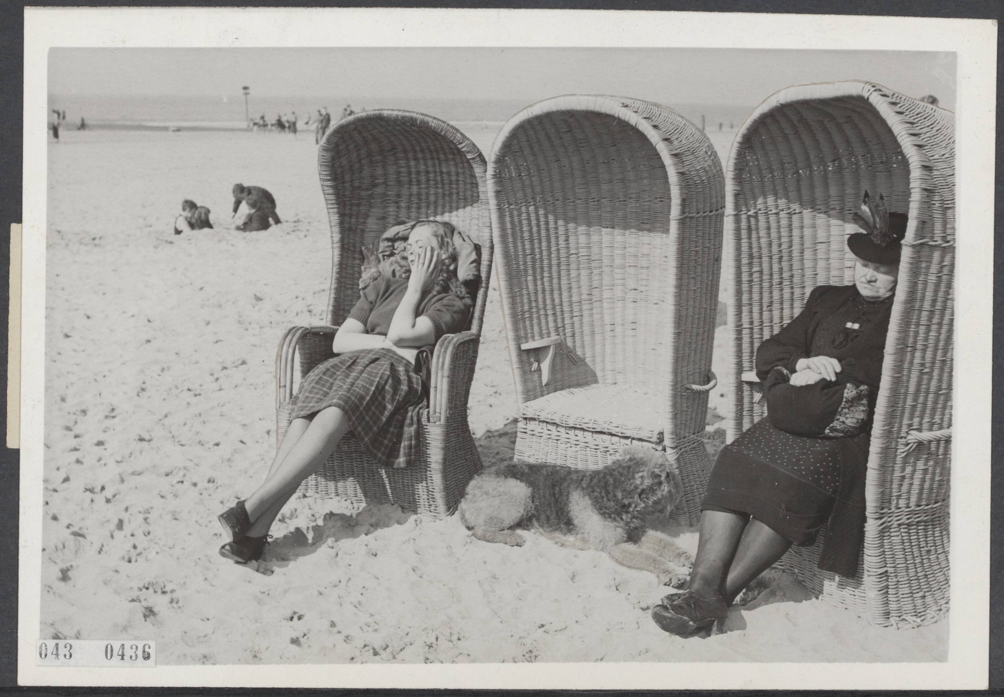 Fotocollectie Elsevier Binnenland — Twee vrouwelijke badgasten, met een hond, in rieten strandstoelen op het strand van Scheveningen — Foto: Groot, [...] de / ANP / Rechtenvrij. Licentie: Set B: Rechtenvrij / Publiek Domein. Bron: Nationaal Archief. http://hdl.handle.net/10648/adf8fbf0-d0b4-102d-bcf8-003048976d84