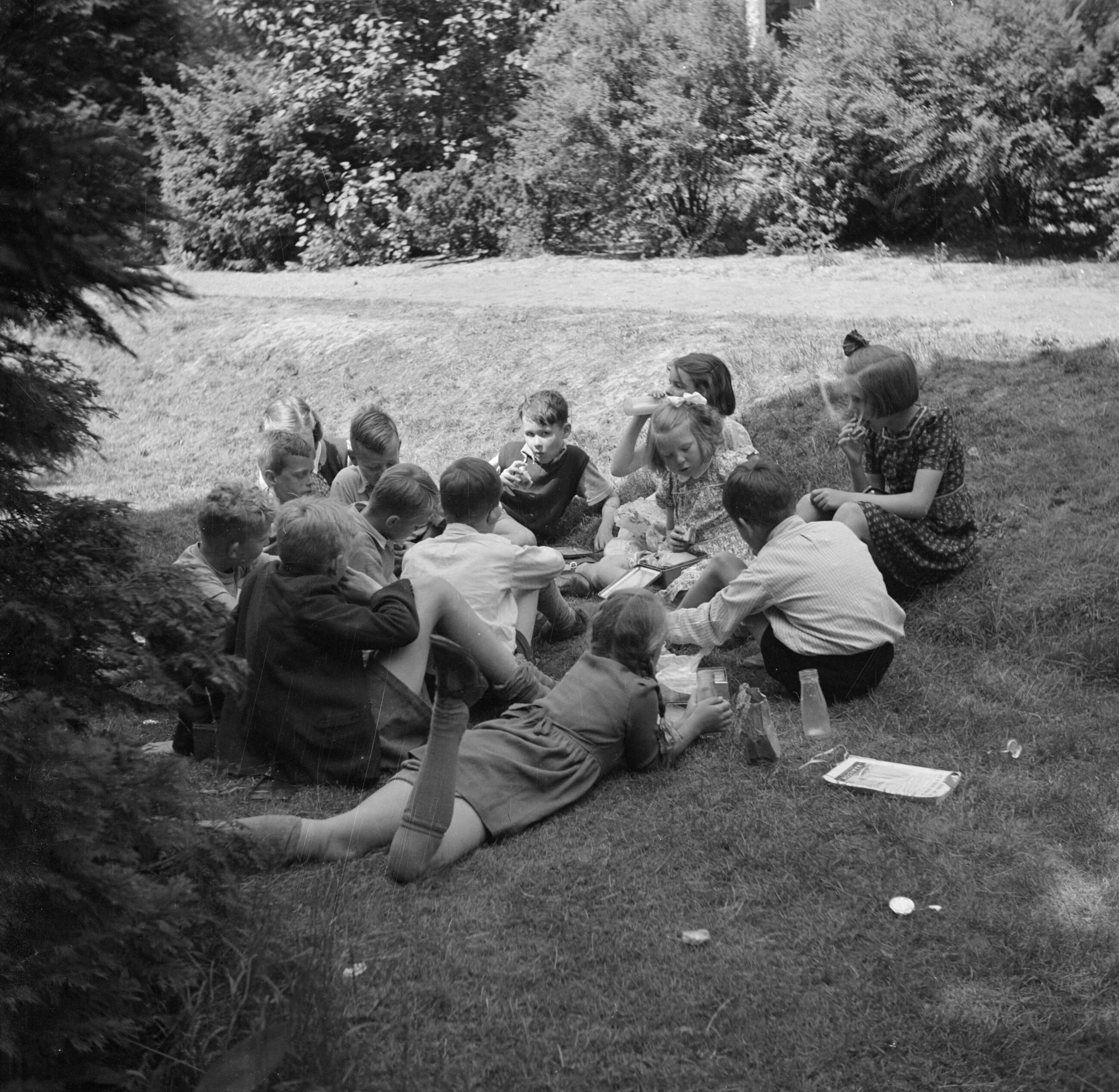 Prinses Beatrix en prinses Irene op de Werkplaats Kindergemeenschap van Kees Boeke te Bilthoven — Prinses Beatrix met andere leerlingen eten boterhammen in de tuin — Foto: Poll, Willem van de. Licentie: Set B: Rechtenvrij / Publiek Domein. Bron: Nationaal Archief. http://hdl.handle.net/10648/aee80f4c-d0b4-102d-bcf8-003048976d84