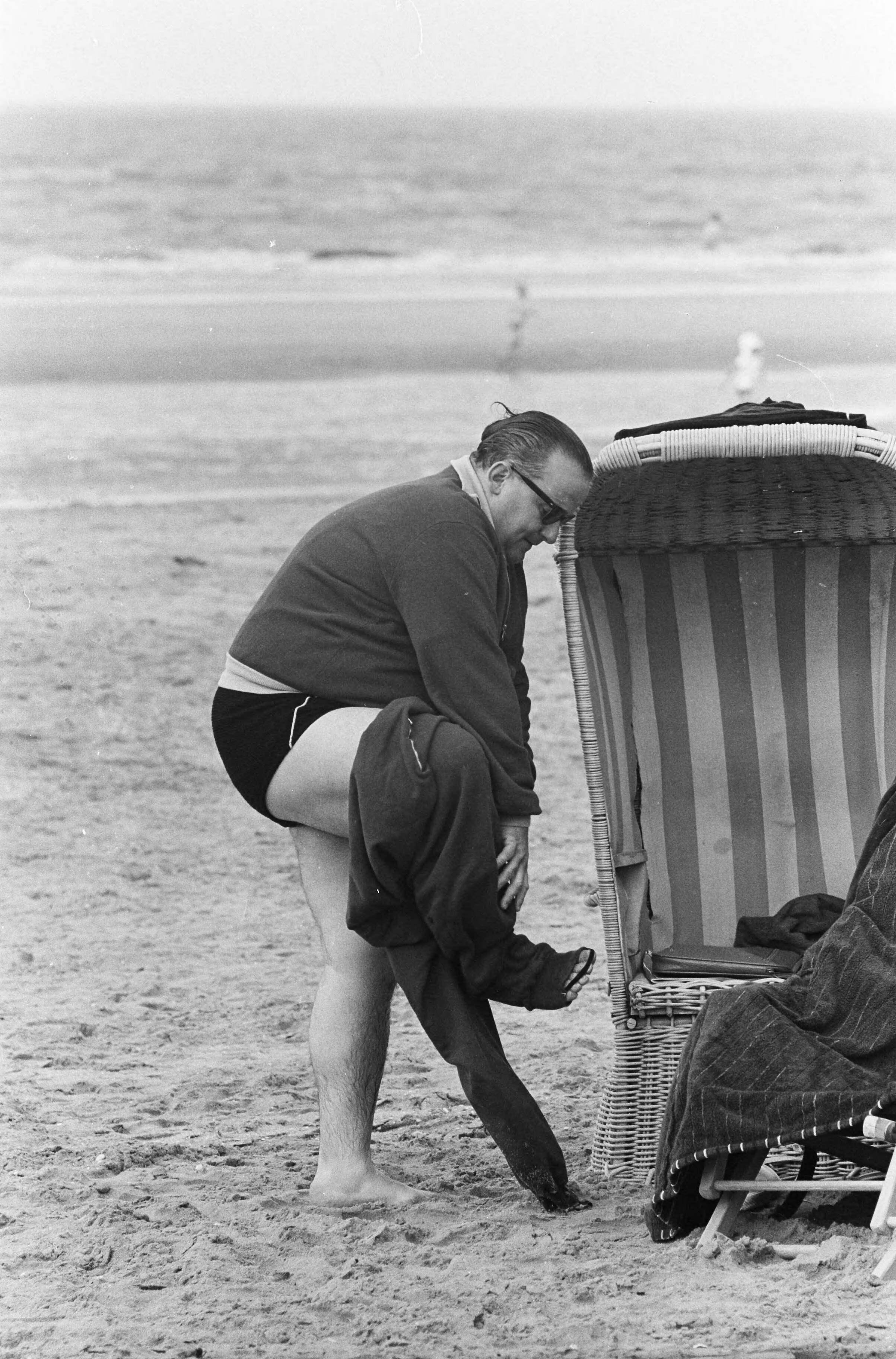 Fotocollectie Anefo — Strand Zandvoort. Corpulente heer probeert zich in broek te wurmen — Foto: Pot, Harry / Anefo. Licentie: Set B: Rechtenvrij / Publiek Domein. Bron: Nationaal Archief. http://hdl.handle.net/10648/aa0b67d0-d0b4-102d-bcf8-003048976d84