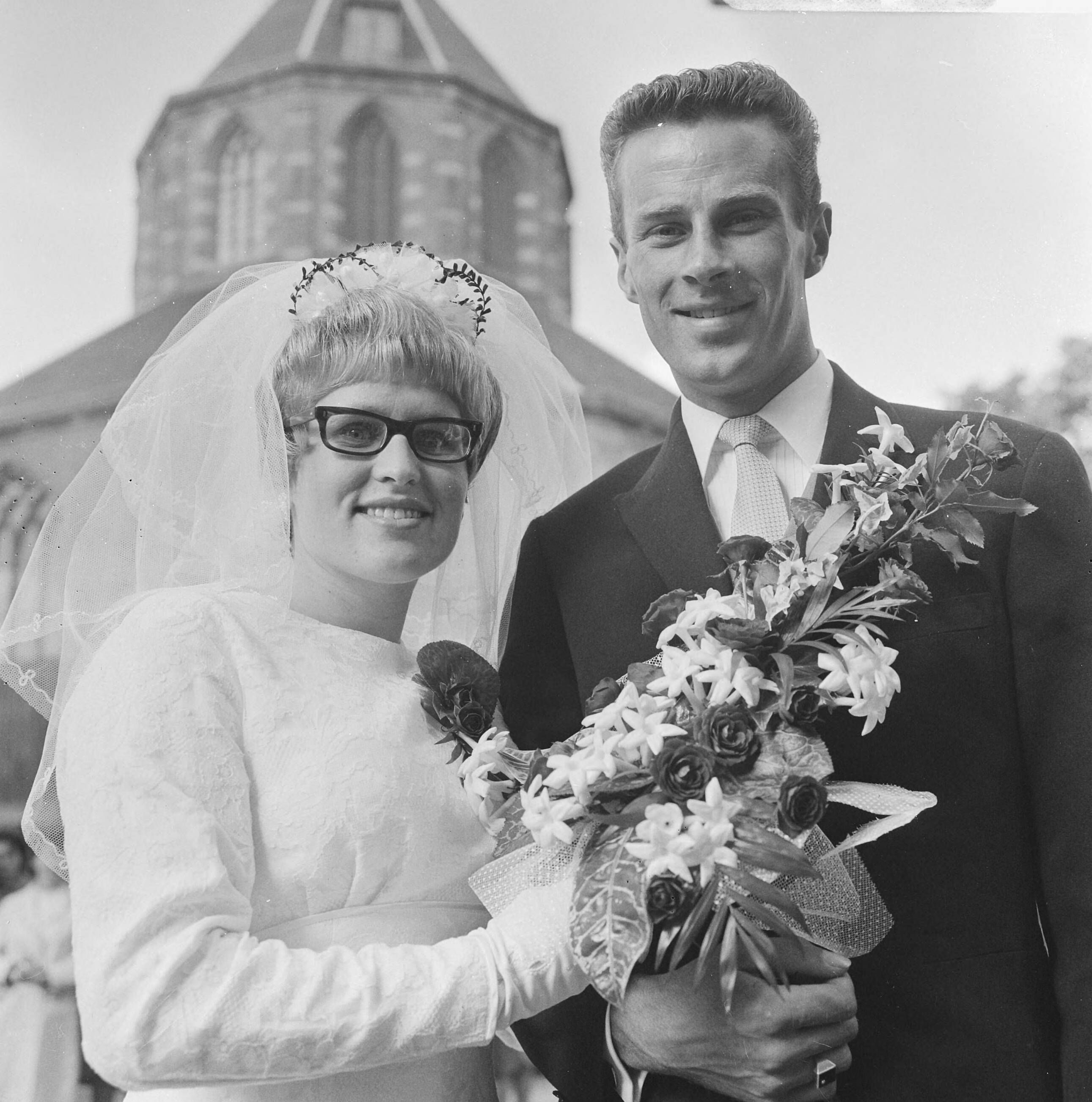 Zwemster Marianne Heemskerk en wielrenner Jaap Oudkerk treden in Naarden in het huwelijk — Het huwelijkspaar voor de kerk van Naarden — Foto: Evers, Joost / Anefo. Licentie: Set B: Rechtenvrij / Publiek Domein. Bron: Nationaal Archief. http://hdl.handle.net/10648/aafc9a74-d0b4-102d-bcf8-003048976d84