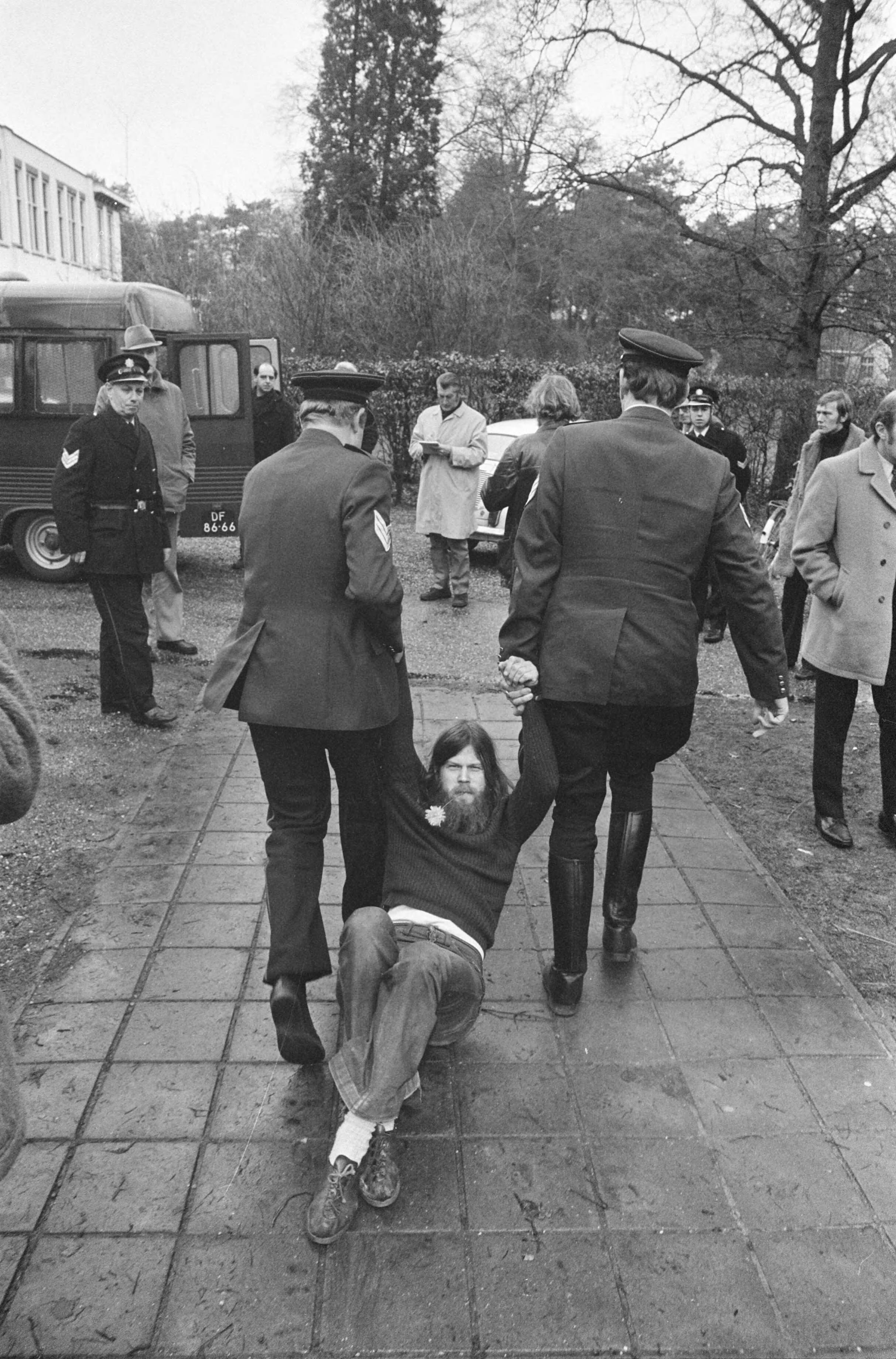 De directiekeet van zwakzinnigeninrichting Dennendal in Den Dolder wordt door de politie ontruimd — Een bezetter wordt weggesleept — Foto: Fotograaf Onbekend / Anefo. Licentie: Set B: Rechtenvrij / Publiek Domein. Bron: Nationaal Archief. http://hdl.handle.net/10648/ac415ca8-d0b4-102d-bcf8-003048976d84