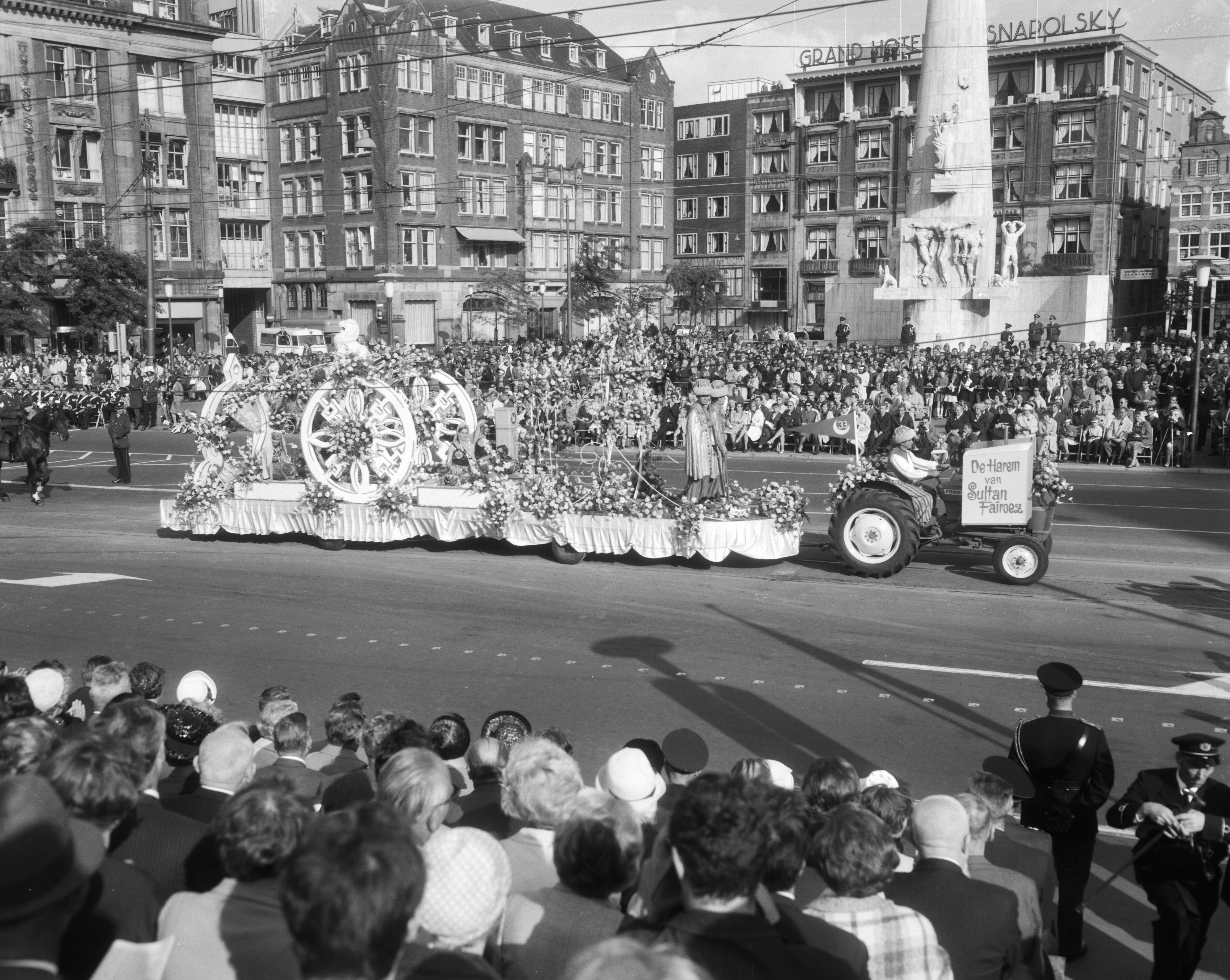 Bloemencorso van Aalsmeer te Amsterdam — Een praalwagen bij de Dam te Amsterdam met op de achtergrond het Nationaal Monument — Foto: Bilsen, Joop van / Anefo. Licentie: Set B: Rechtenvrij / Publiek Domein. Bron: Nationaal Archief. http://hdl.handle.net/10648/aafaf5a2-d0b4-102d-bcf8-003048976d84