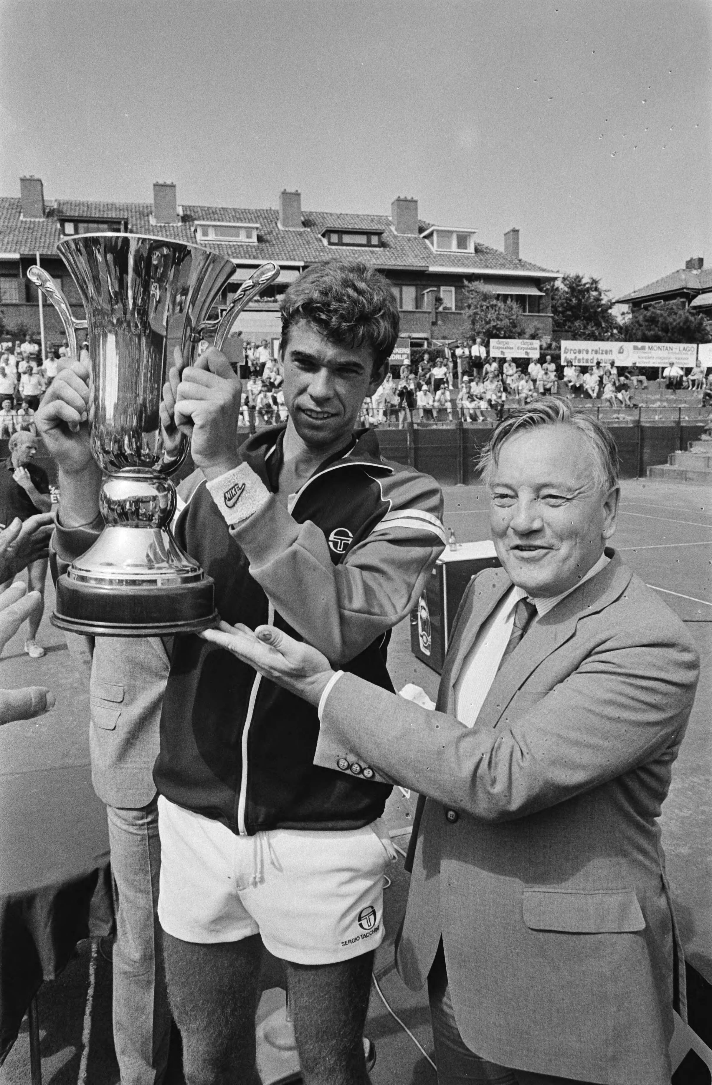 Nederlands Kampioenschap Tennis op de METS-banen in Scheveningen — Nederlands kampioen Michiel Schapers met beker, rechts staatssecretaris Van der Reijden (WVC) — Foto: Antonisse, Marcel / Anefo. Licentie: Set B: Rechtenvrij / Publiek Domein. Bron: Nationaal Archief. http://hdl.handle.net/10648/ad2c66bc-d0b4-102d-bcf8-003048976d84