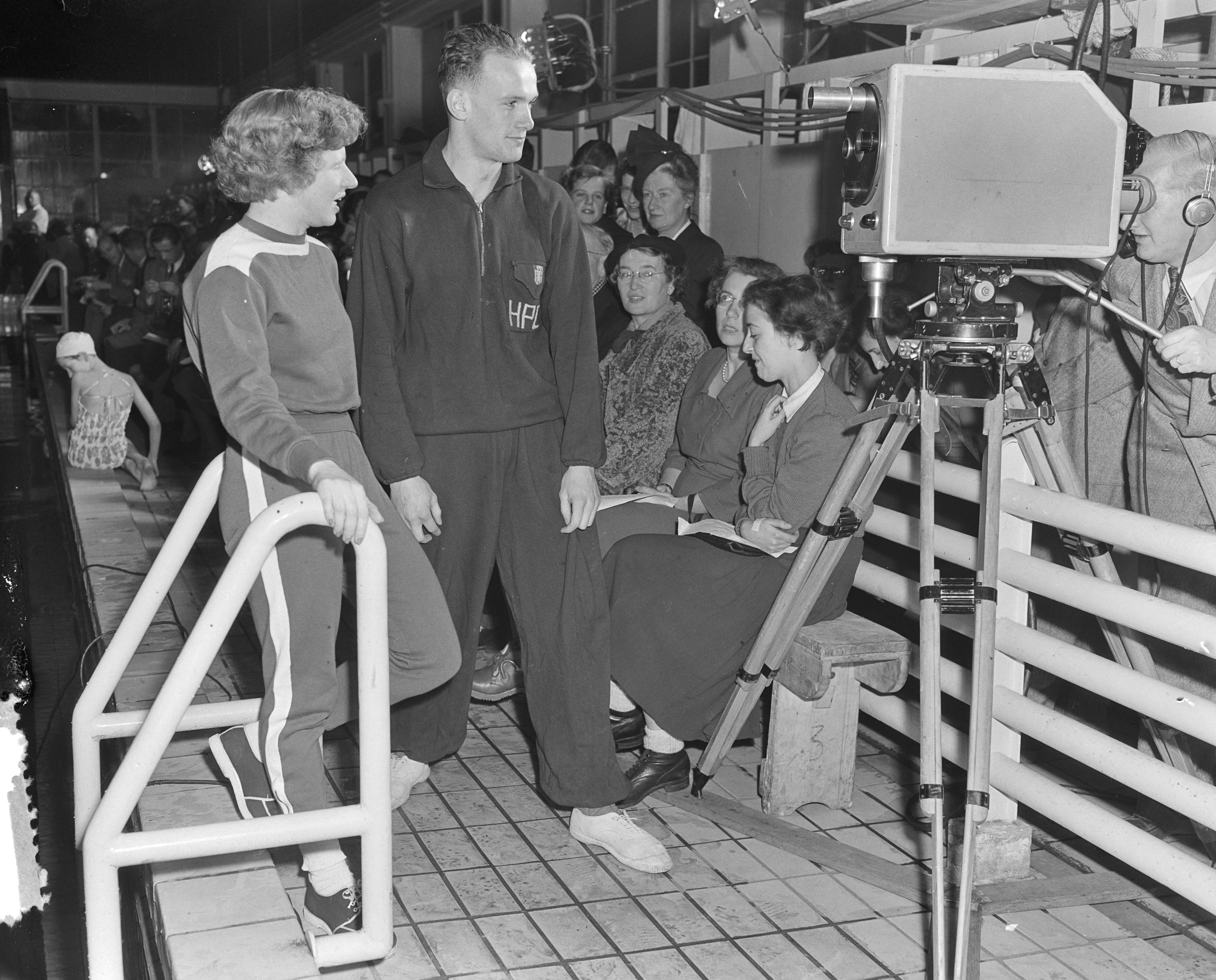 Fotocollectie Anefo — Ïn het zwemstadion te Naarden werden Nationale zwemwedstrijden georganiseerd door de AVRO. Deze wedstrijden werden in een directe televisie-uitzending uitgezonden. Irma Schuhmacher en Joris Tjebbes voor de camera om aan het televisiepubliek te worden voorgesteld — Foto: Pot, Harry / Anefo. Licentie: Set B: Rechtenvrij / Publiek Domein. Bron: Nationaal Archief. http://hdl.handle.net/10648/a8f4166c-d0b4-102d-bcf8-003048976d84