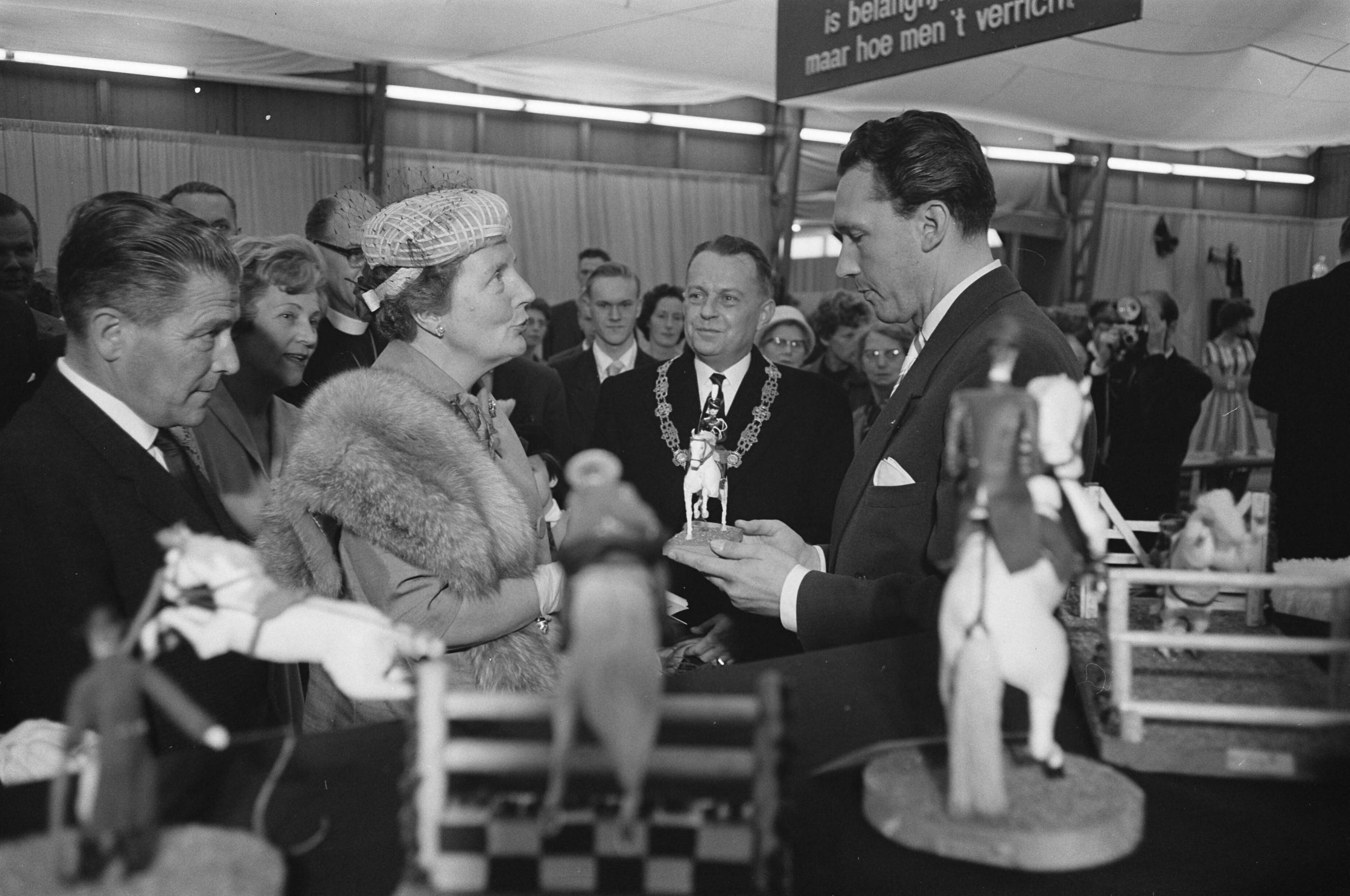 Fotocollectie Anefo — Koningin Juliana bezoekt tentoonstelling "Nu .... Breda 61 ". In de hobbyhal bood de heer H. van der Kroon haar een door hem zeil vervaardigd paardje met ruiter van leer aan, bestemd voor prinses Marijke — Foto: Pot, Harry / Anefo. Licentie: Set B: Rechtenvrij / Publiek Domein. Bron: Nationaal Archief. http://hdl.handle.net/10648/a9dd1894-d0b4-102d-bcf8-003048976d84