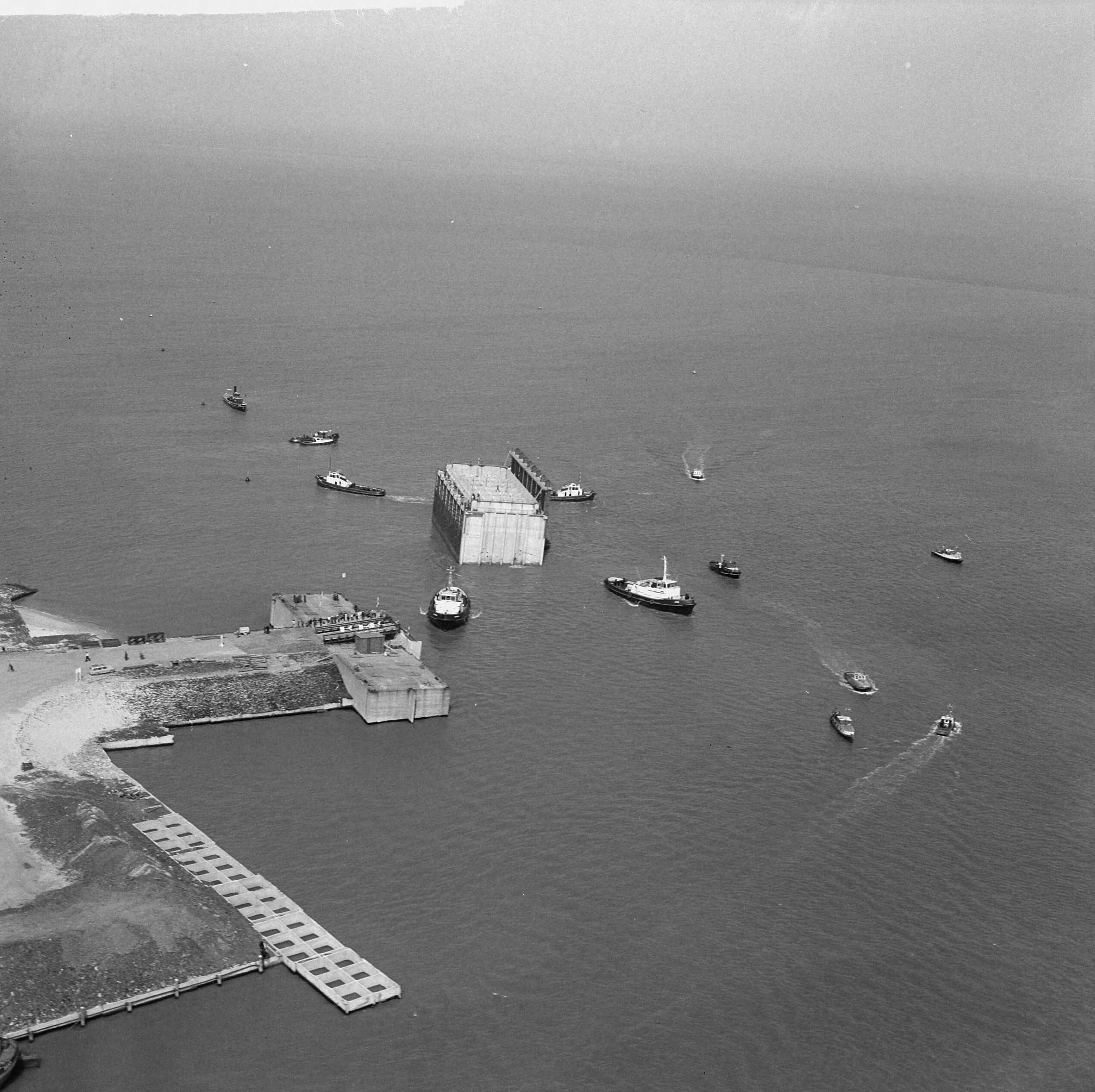 Fotocollectie Anefo — Luchtopnamen. Invaren van caissons in het Veerse Gat — Foto: Slagboom, Anton / Anefo. Licentie: Set B: Rechtenvrij / Publiek Domein. Bron: Nationaal Archief. http://hdl.handle.net/10648/a9d111c0-d0b4-102d-bcf8-003048976d84