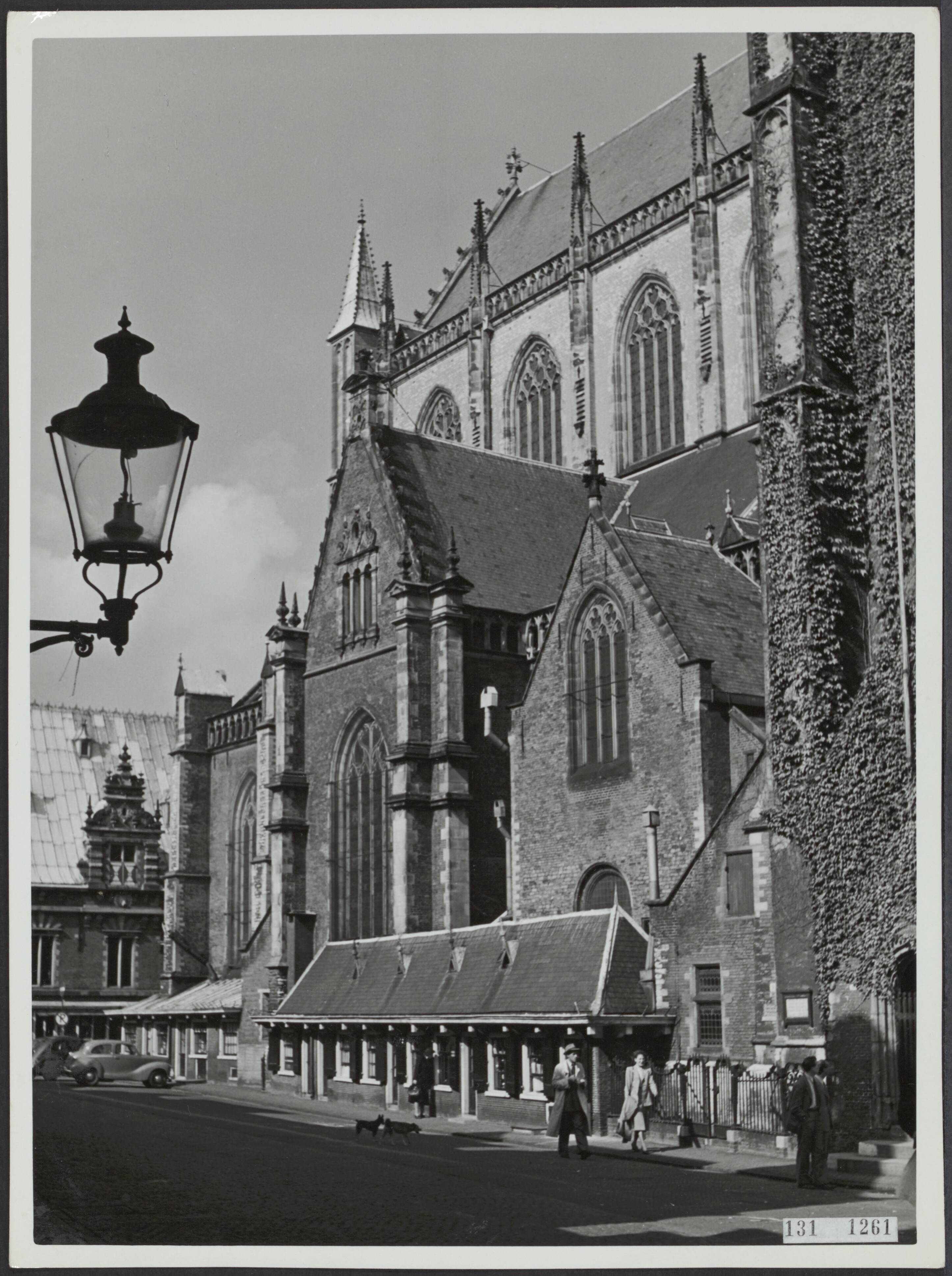 Fotocollectie Rijksvoorlichtingsdienst Eigen — Haarlem. St. Bavokerk: gezicht op de zuidzijde van het schip met de gevel van de fontkapel en huisjes die tegen de kerk zijn aangebouwd. Links een lantaarn die aan een muur is bevestigd — Foto: Rijksvoorlichtingsdienst (RVD). Licentie: Set B: Rechtenvrij / Publiek Domein. Bron: Nationaal Archief. http://hdl.handle.net/10648/af51ef34-d0b4-102d-bcf8-003048976d84