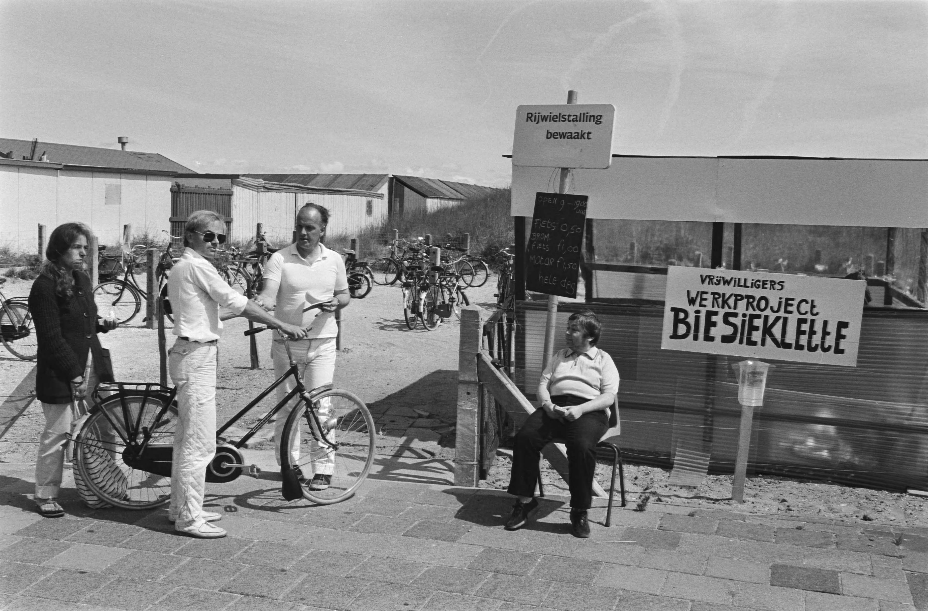 Fietsenstalling bemand door werklozen, met behoud van uitkering in Scheveningen — Fietser bij de stalling met het bord "Vrijwilligers werkproject Biesieklette" — Foto: Antonisse, Marcel / Anefo. Licentie: Set B: Rechtenvrij / Publiek Domein. Bron: Nationaal Archief. http://hdl.handle.net/10648/ad2be8b8-d0b4-102d-bcf8-003048976d84