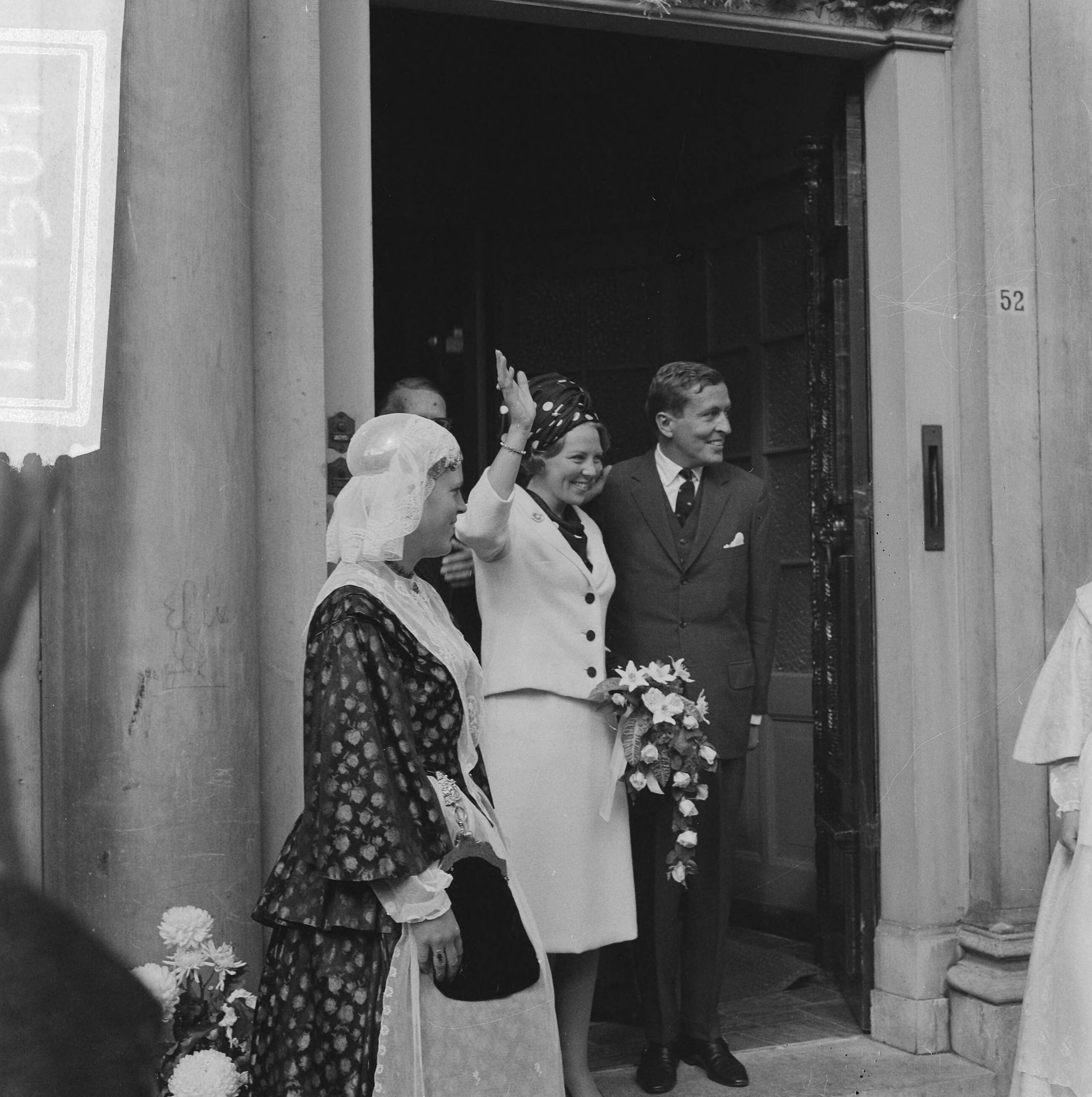 Bezoek van prinses Beatrix en Claus von Amsberg aan de drie noordelijke provincies — Bezoek prinses Beatrix en haar verloofde Claus von Amsberg aan Leeuwarden, zwaaiend in de ingang van het Provinciehuis. Aan weerszijden meisjes in Friese klederdracht — Foto: Kroon, Ron / Anefo. Licentie: Set B: Rechtenvrij / Publiek Domein. Bron: Nationaal Archief. http://hdl.handle.net/10648/aabf01aa-d0b4-102d-bcf8-003048976d84