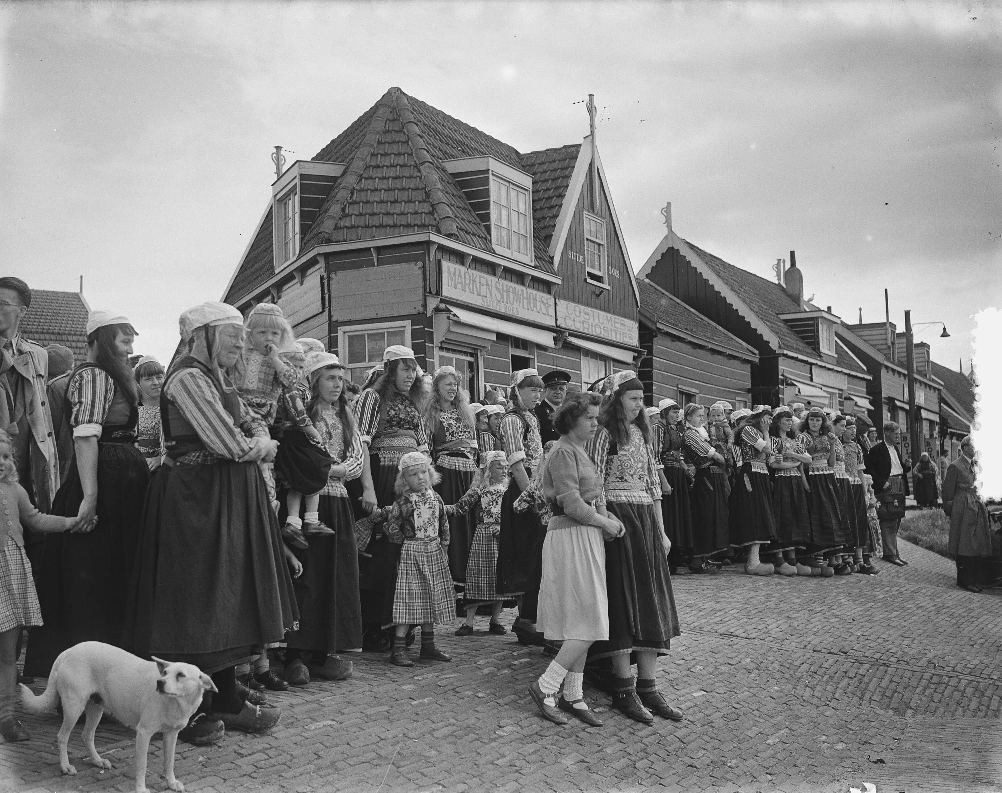 Nieuwe burgemeester van Marken B.C. van Hout — Installatie van de nieuwe burgemeester van Marken B.C. van Hout . Publiek in klederdracht staat op de dijk voor de souvenirwinkel van Sijtje Boes — Foto: Bilsen, Joop van / Anefo. Licentie: Set B: Rechtenvrij / Publiek Domein. Bron: Nationaal Archief. http://hdl.handle.net/10648/a8ff2aac-d0b4-102d-bcf8-003048976d84