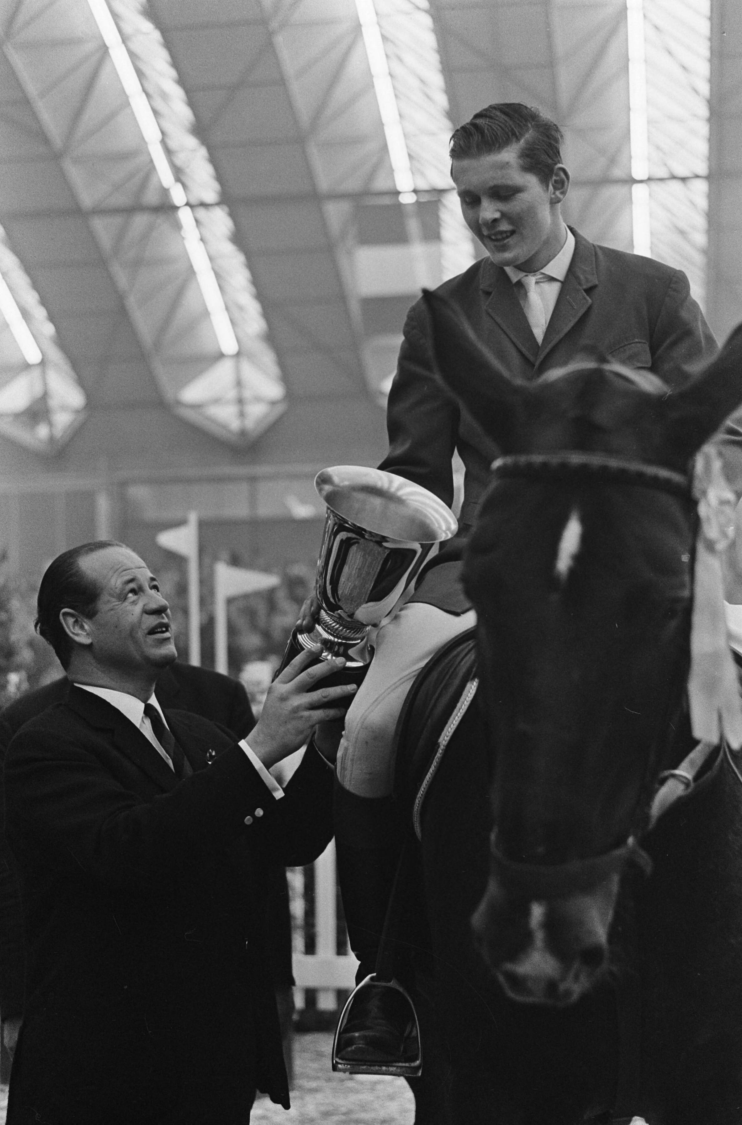 Jumping Amsterdam 1965 in de RAI te Amsterdam — Freddy Heineken terwijl hij beker van de Grote Prijs van Nederland aan de Duitse ruiter Gert Wilftang overhandigt — Foto: Fotograaf Onbekend / Anefo. Licentie: Set B: Rechtenvrij / Publiek Domein. Bron: Nationaal Archief. http://hdl.handle.net/10648/aac9213a-d0b4-102d-bcf8-003048976d84