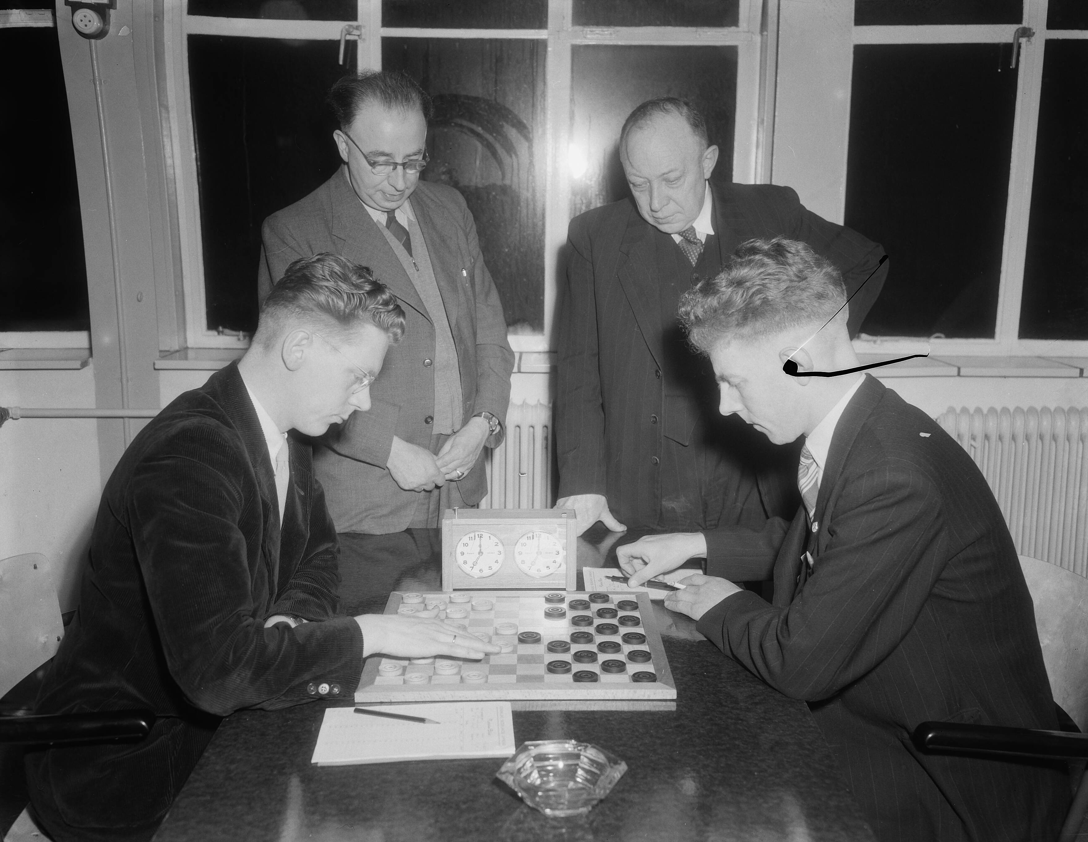 Fotocollectie Anefo — Nederlands kampioenschap Dammen in Utrecht. J.H. Ansems (Amsterdam) tegen A. van de Berg (Gouda). Achter de tafel links de wedstrijdleider van de Kon. Ned. Dam Bond en rechts de wedstrijleider van de Utrechtse Provinciale Dam Bond — Foto: Duinen, G.W. van / Anefo. Licentie: Set B: Rechtenvrij / Publiek Domein. Bron: Nationaal Archief. http://hdl.handle.net/10648/a91da7c0-d0b4-102d-bcf8-003048976d84