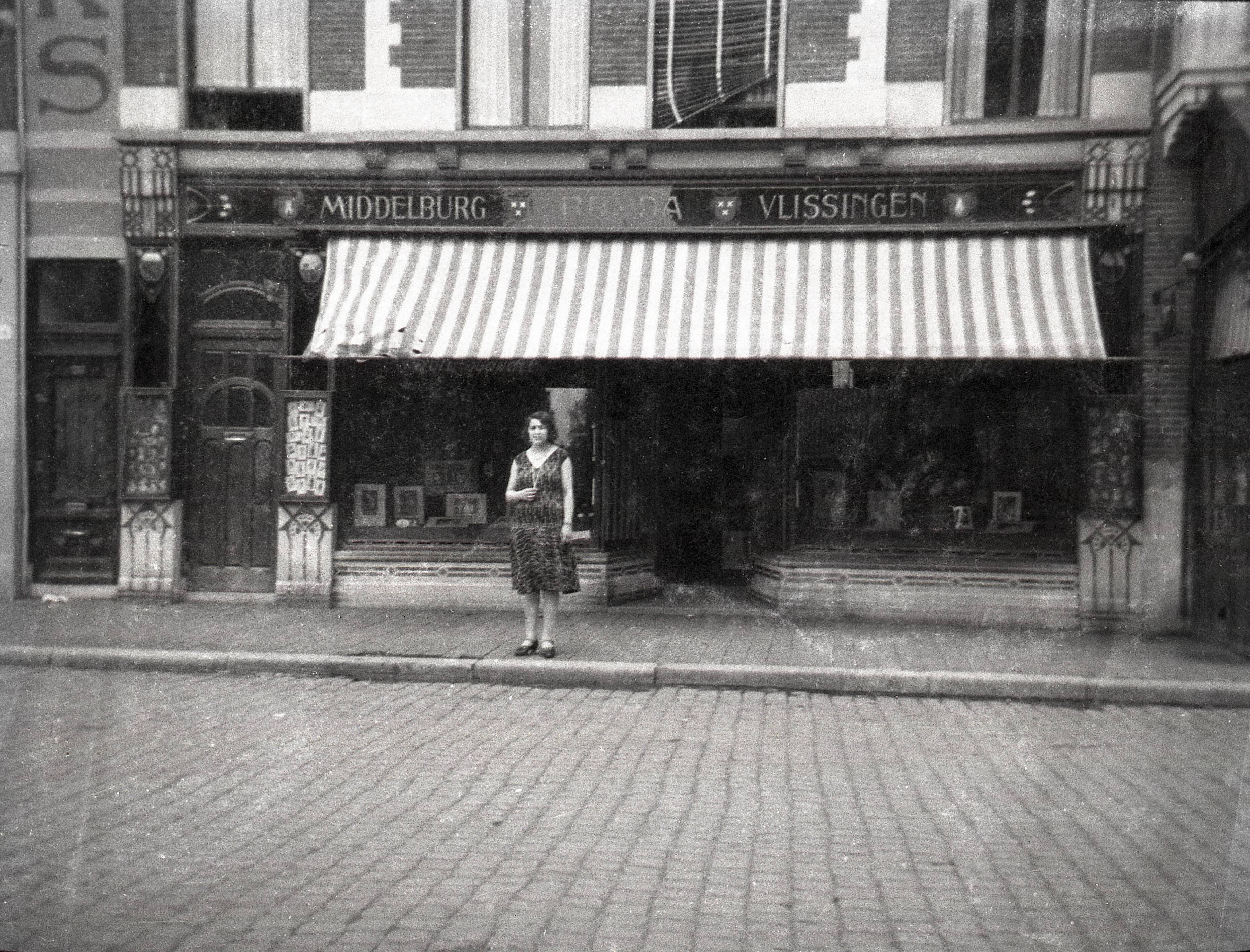 Portretten, "Economie, handel, industrie, bouw, arbeid", Verkeer, "Geluid, beeld, fotografie, publiciteit", "Topografie, plaatsen op naam" — Fietsen in Nederland. Een jonge vrouw staat op het met kinderhoofdjes geplaveide Van Coothplein te Breda voor de etalage van 'Atelier Anton Henning', blijkens de opschriften tevens met vestigingen van Middelburg en Vlissingen. De firma van fotograaf Henning was bekend om zijn portretten, die tevens zichtbaar zijn in uitstalkasten aan de gevel. Omstreeks 1928. De foto is afkomstig uit de collectie van portretfotograaf bekend onder de naam 'Atelier Anton Henning'. — Foto: Fotograaf onbekend / Fotobureau onbekend / Rechtenvrij (05889). Licentie: Set B: Rechtenvrij / Publiek Domein. Bron: Nationaal Archief. http://hdl.handle.net/10648/35429da6-64bb-a382-e063-6df0900a6686