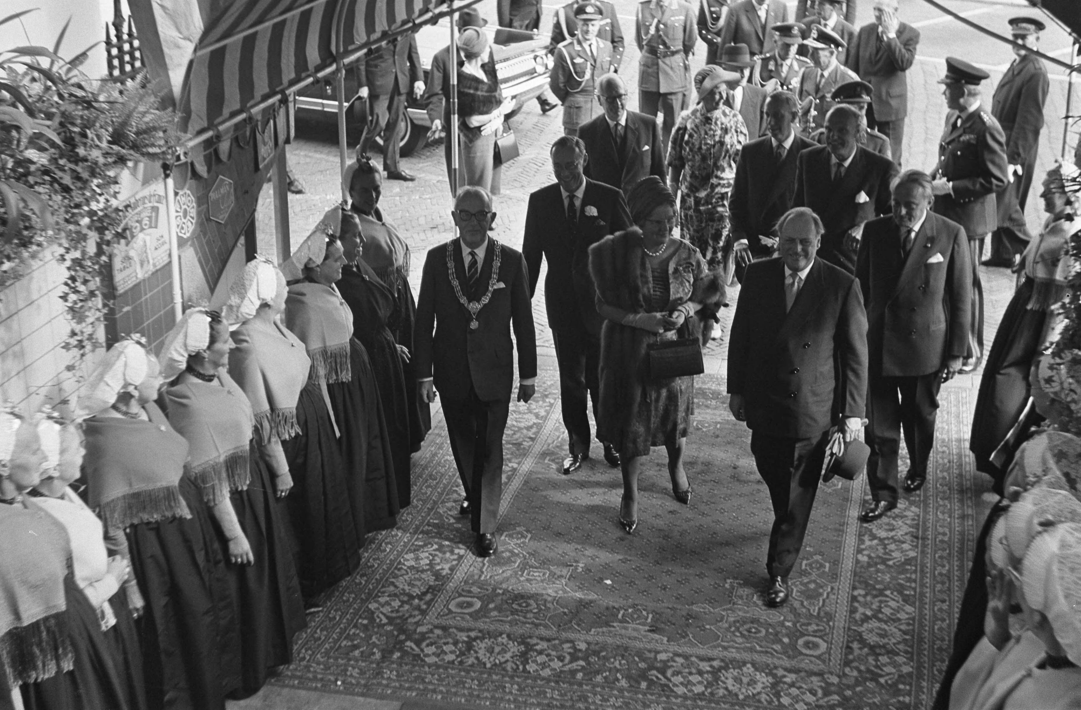 Staatsbezoek van koning Olav van Noorwegen aan Nederland — Bezoek koning Olav van Noorwegen aan Den Haag. Geflankeerd door twee rijen, in klederdracht gehulde Scheveningse vissersvrouwen, betreden de koninklijke gasten het Kürhaus — Foto: Nijs, Jac. de / Anefo. Licentie: Set B: Rechtenvrij / Publiek Domein. Bron: Nationaal Archief. http://hdl.handle.net/10648/aa7872e4-d0b4-102d-bcf8-003048976d84