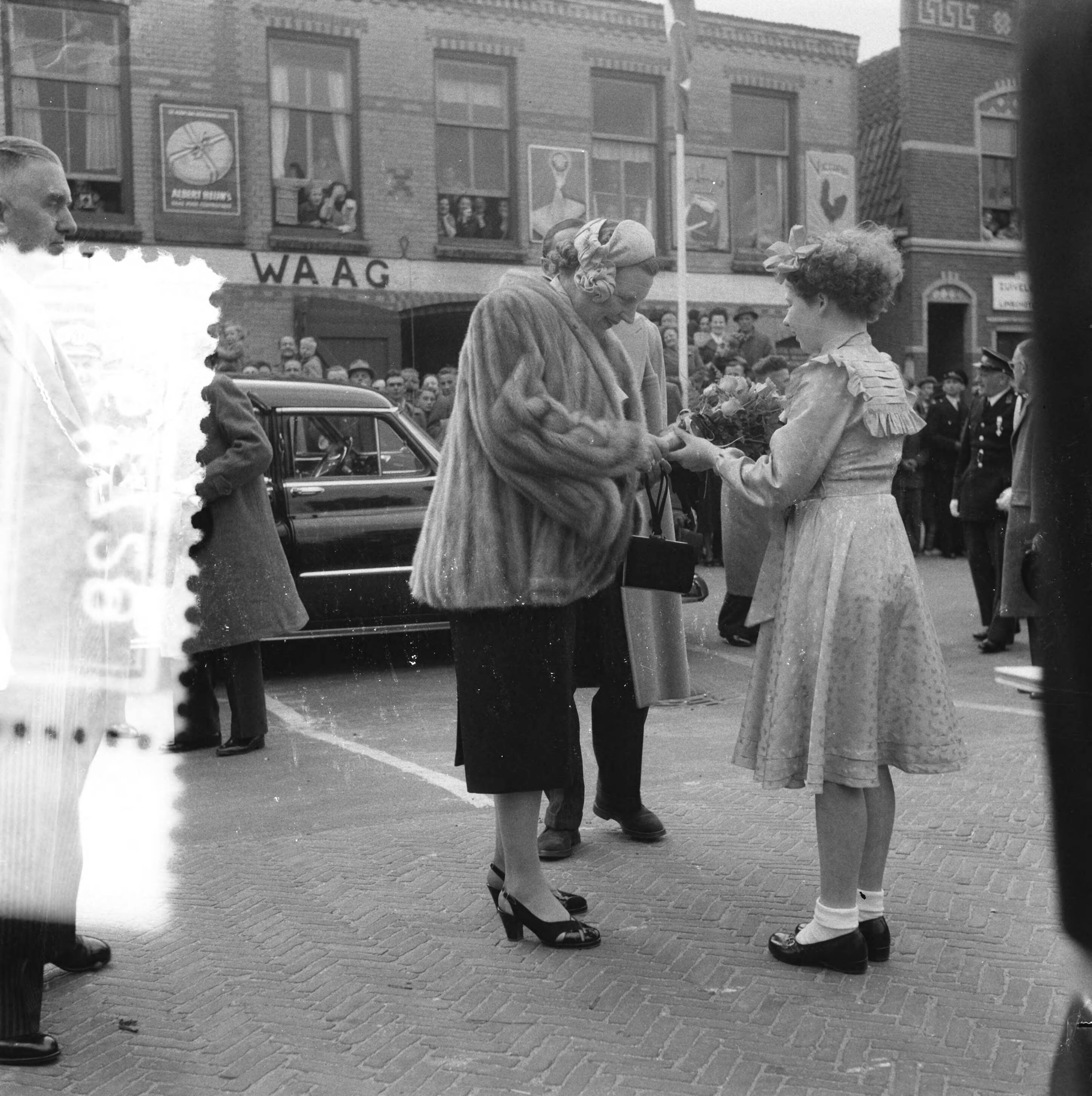 Koninklijk bezoek aan 15 gemeentes in Zuid-Holland (Rijnstreek en Merengebied) — Koningin Juliana en prins Bernhard bezoeken de kaasmarkt in Woerden. De 12-jarige Johanna van Angeren biedt de koningin bloemen aan — Foto: Creijton, […] / Anefo. Licentie: Set B: Rechtenvrij / Publiek Domein. Bron: Nationaal Archief. http://hdl.handle.net/10648/a9222a20-d0b4-102d-bcf8-003048976d84